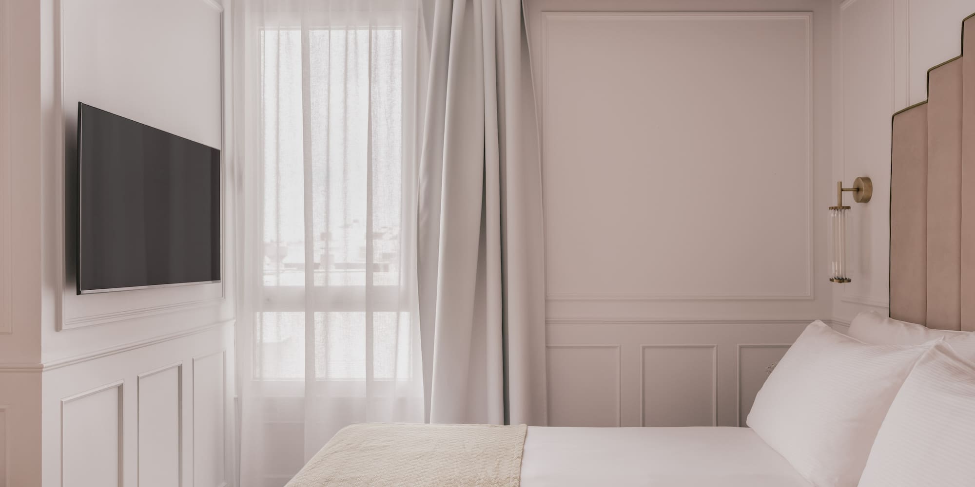 Elegant bedroom with white paneled walls, mounted TV, and cozy bed.