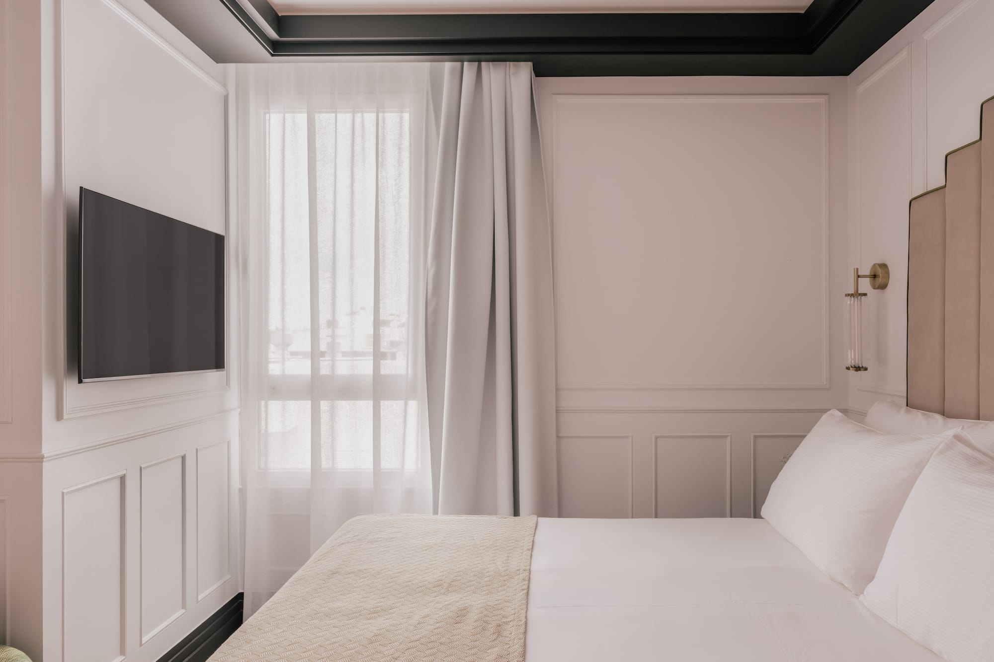 Elegant bedroom with white paneled walls, mounted TV, and cozy bed.