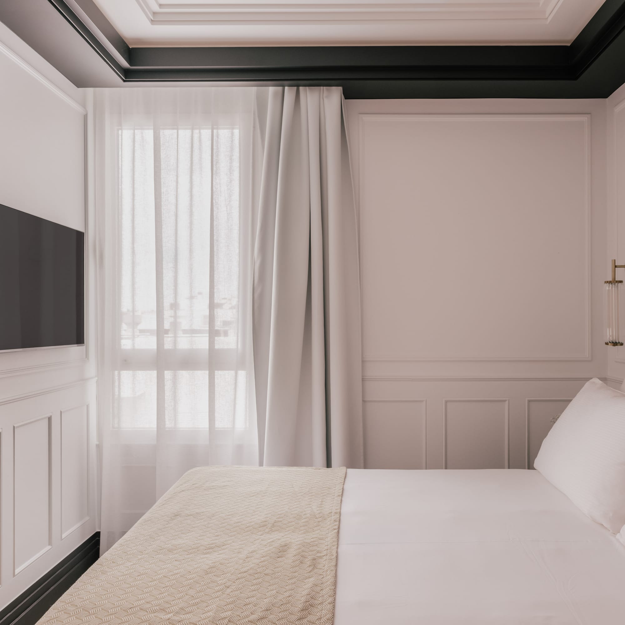 Elegant bedroom with white paneled walls, mounted TV, and cozy bed.
