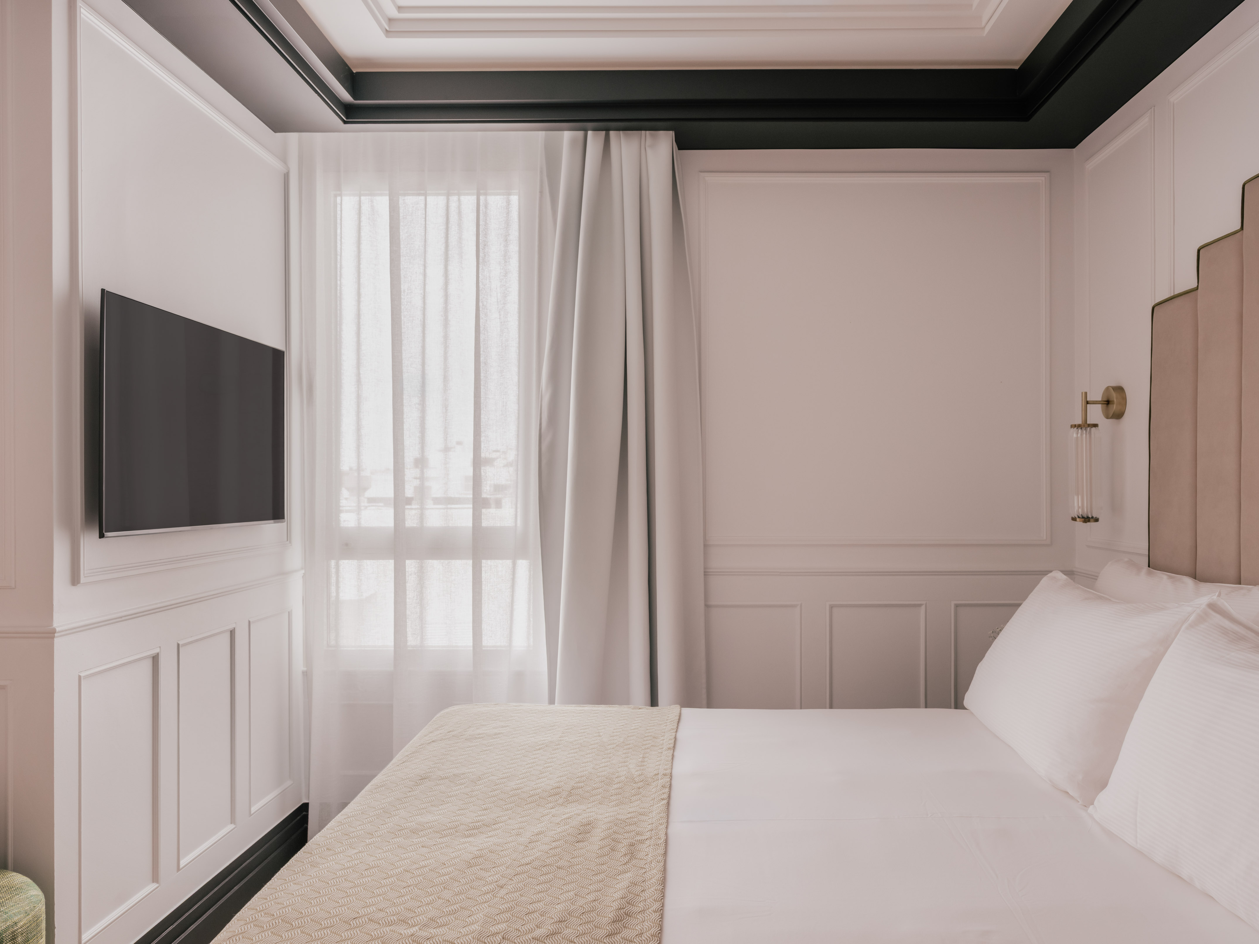Elegant bedroom with white paneled walls, mounted TV, and cozy bed.