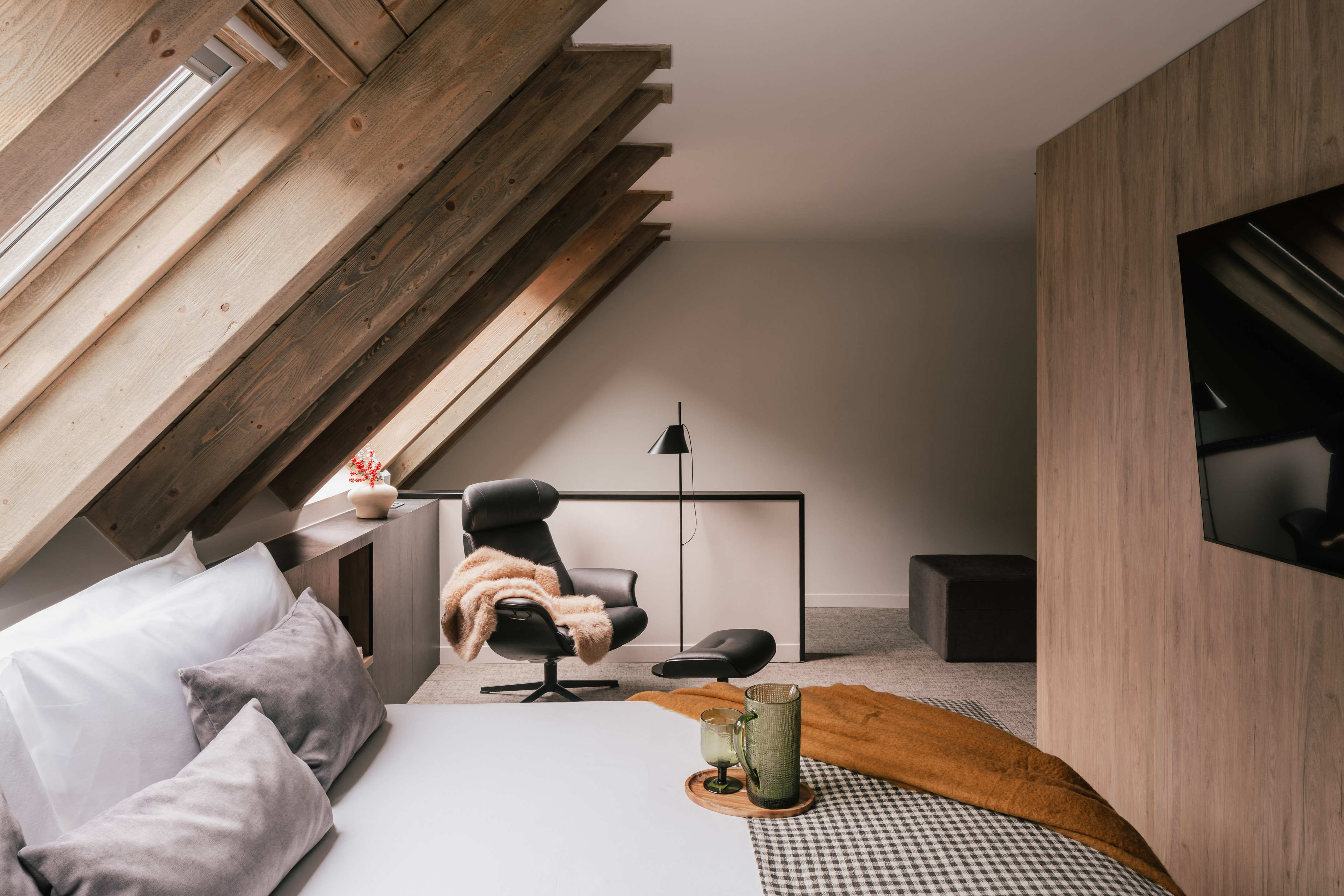 Cozy attic bedroom with exposed wooden beams, skylight, bed, and armchair.