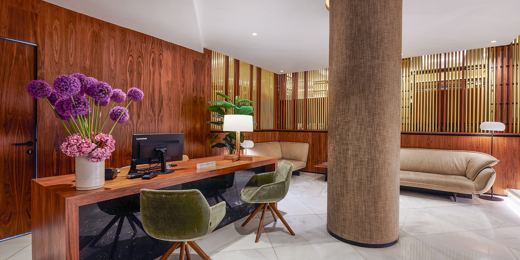 Hotel reception area with wood walls, marble floor, desk, and green chairs.