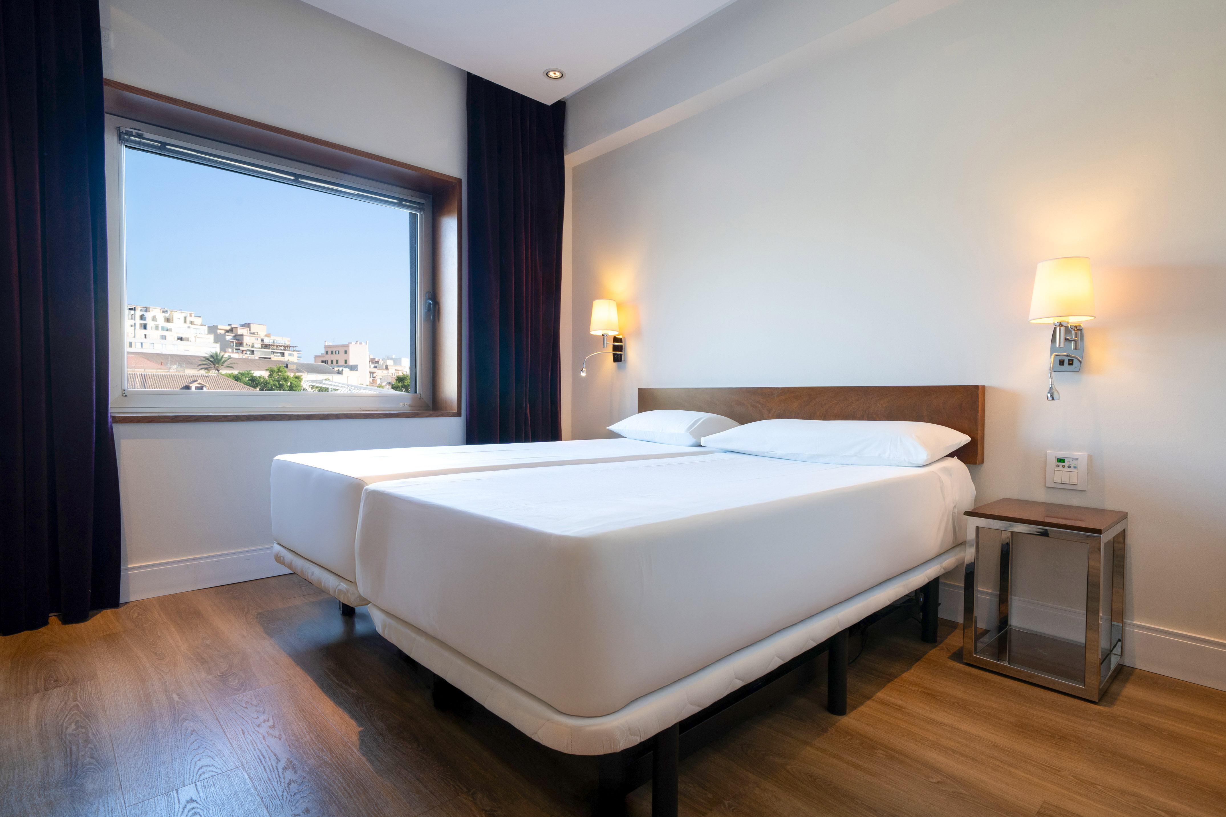 Modern hotel bedroom with twin beds, city view, and wood floor.