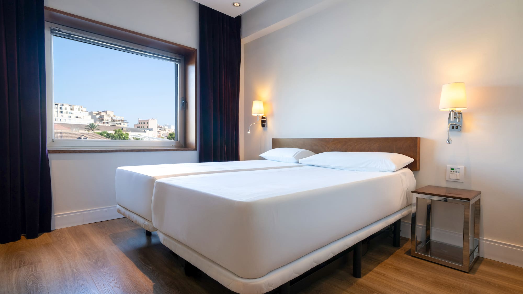 Modern hotel bedroom with twin beds, city view, and wood floor.