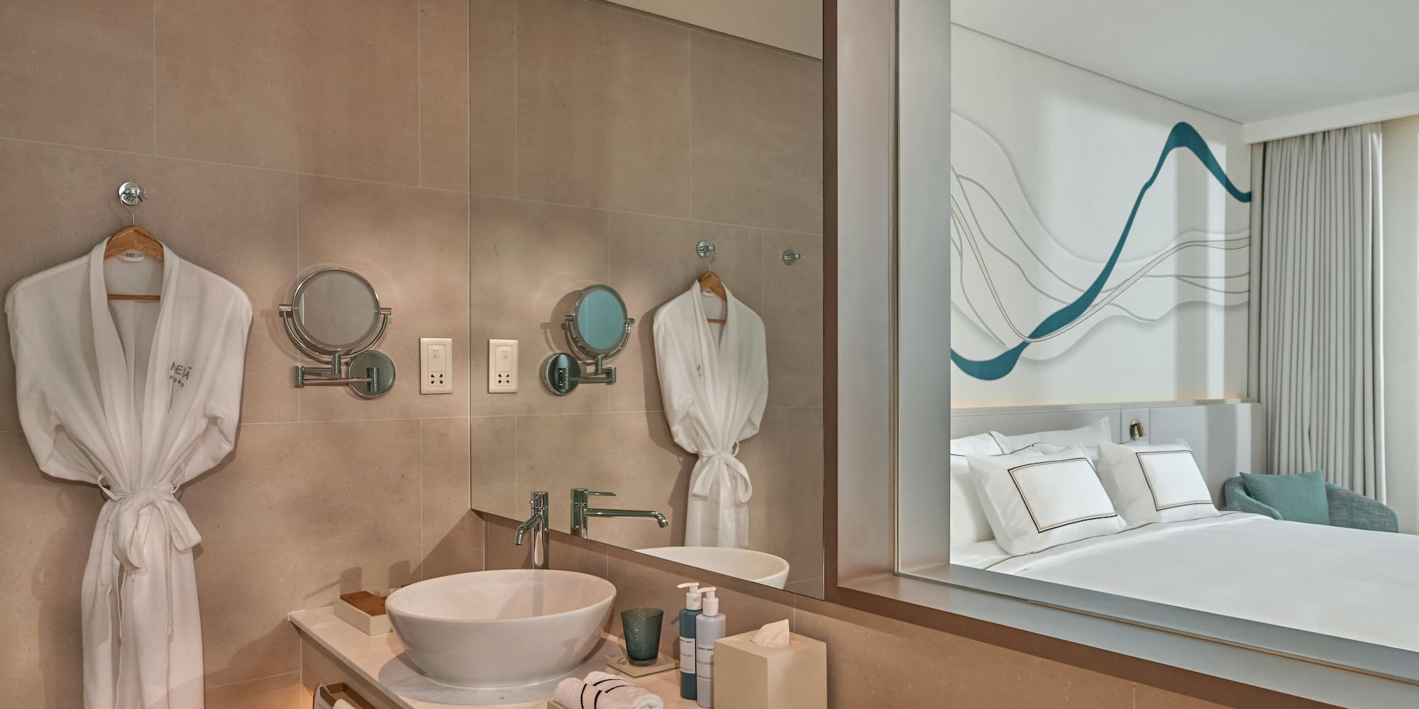 Contemporary hotel bathroom vanity with robes, mirror reflecting modern bedroom.