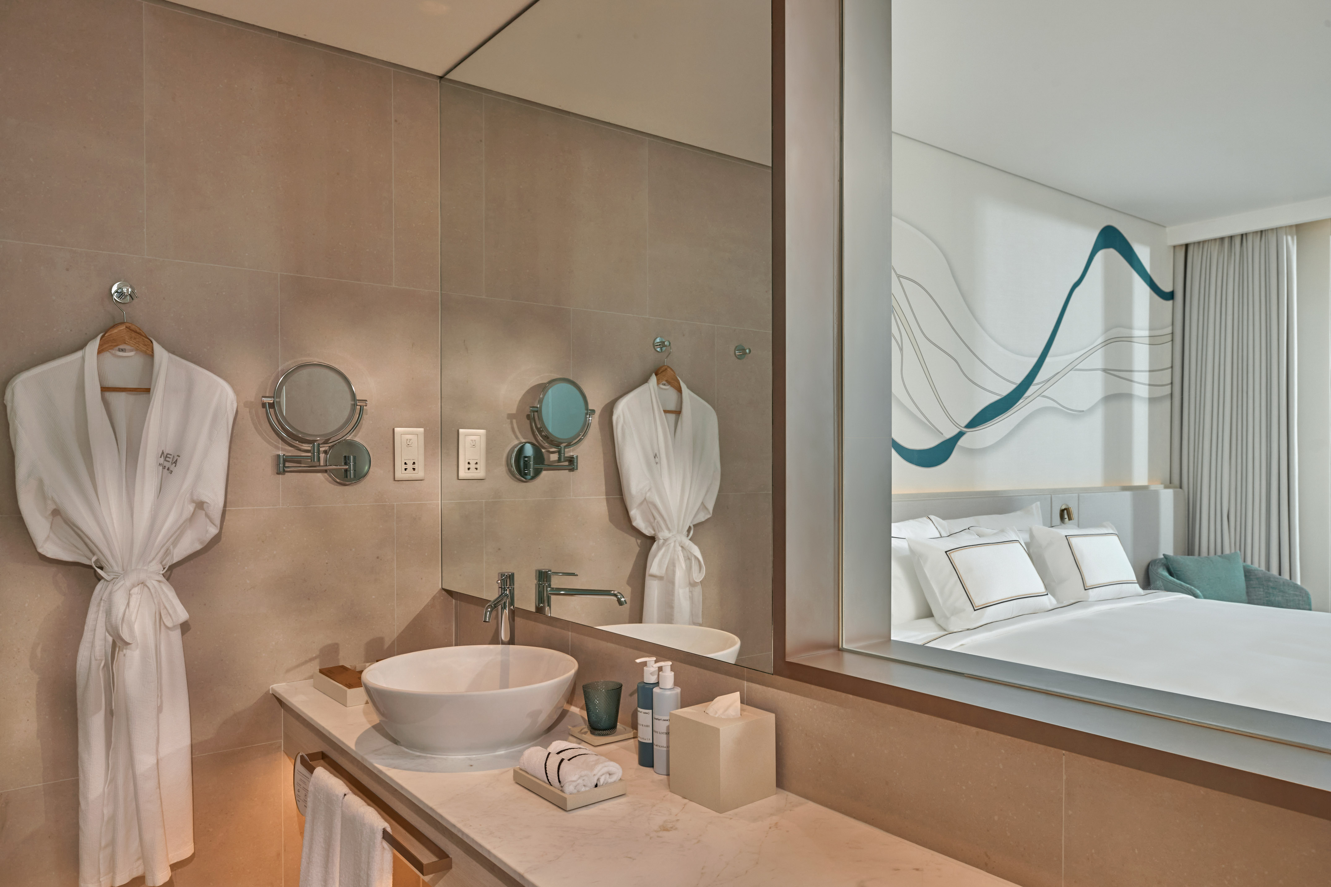 Contemporary hotel bathroom vanity with robes, mirror reflecting modern bedroom.