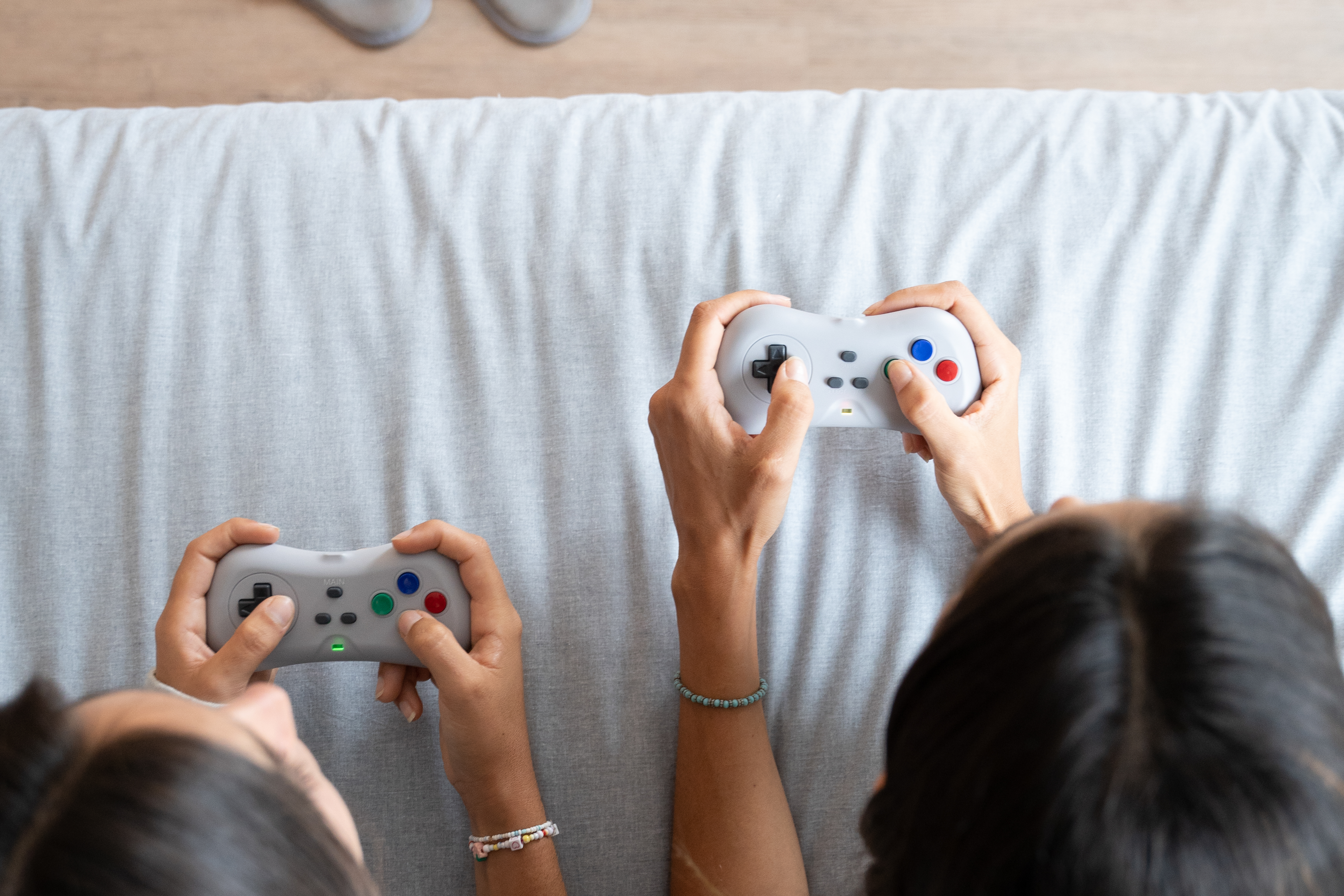 Two people playing video games with retro controllers on a light grey surface.