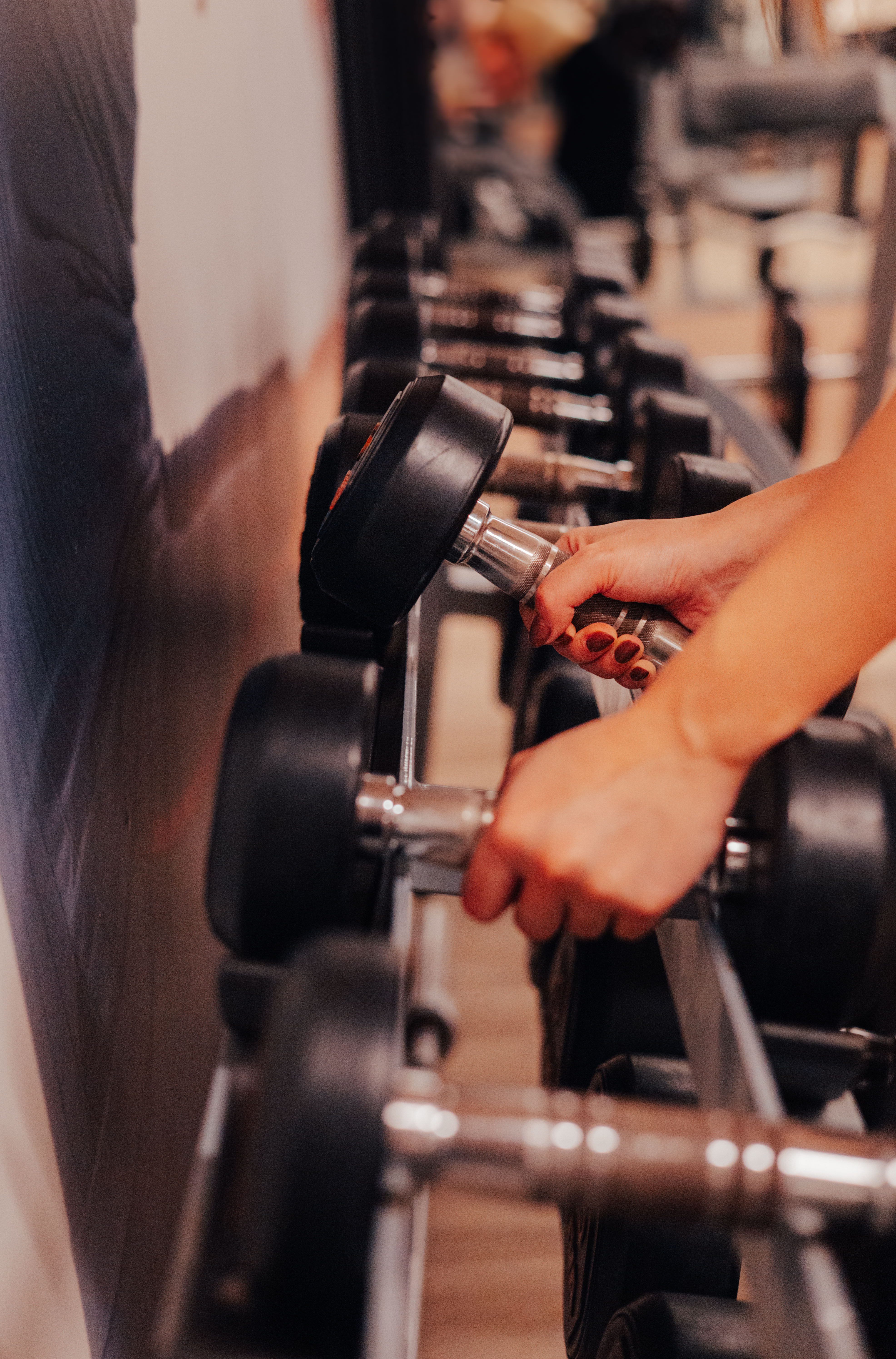Woman's hands gripping a dumbbell on a weight rack in a gym.