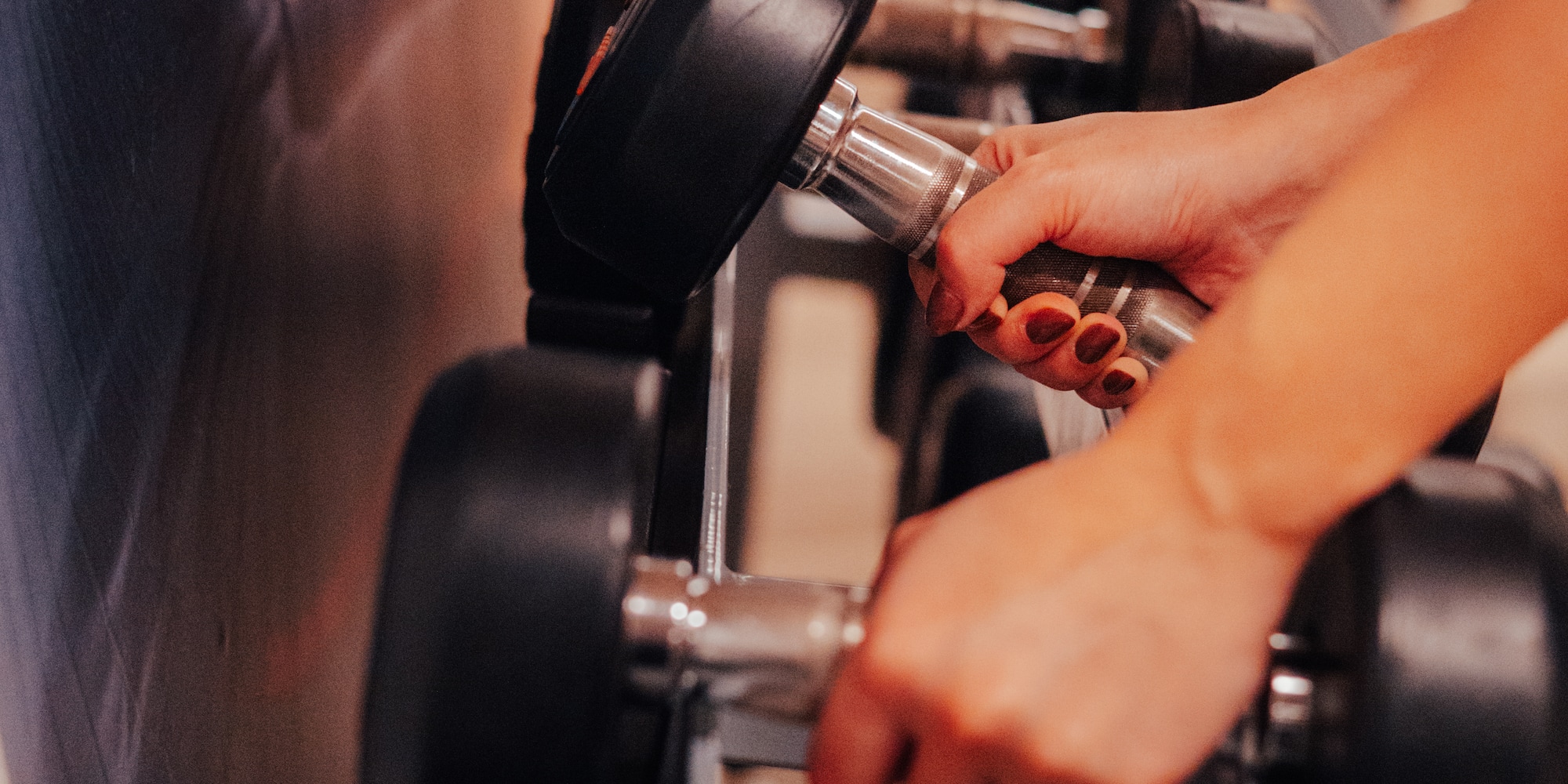 Woman's hands gripping a dumbbell on a weight rack in a gym.