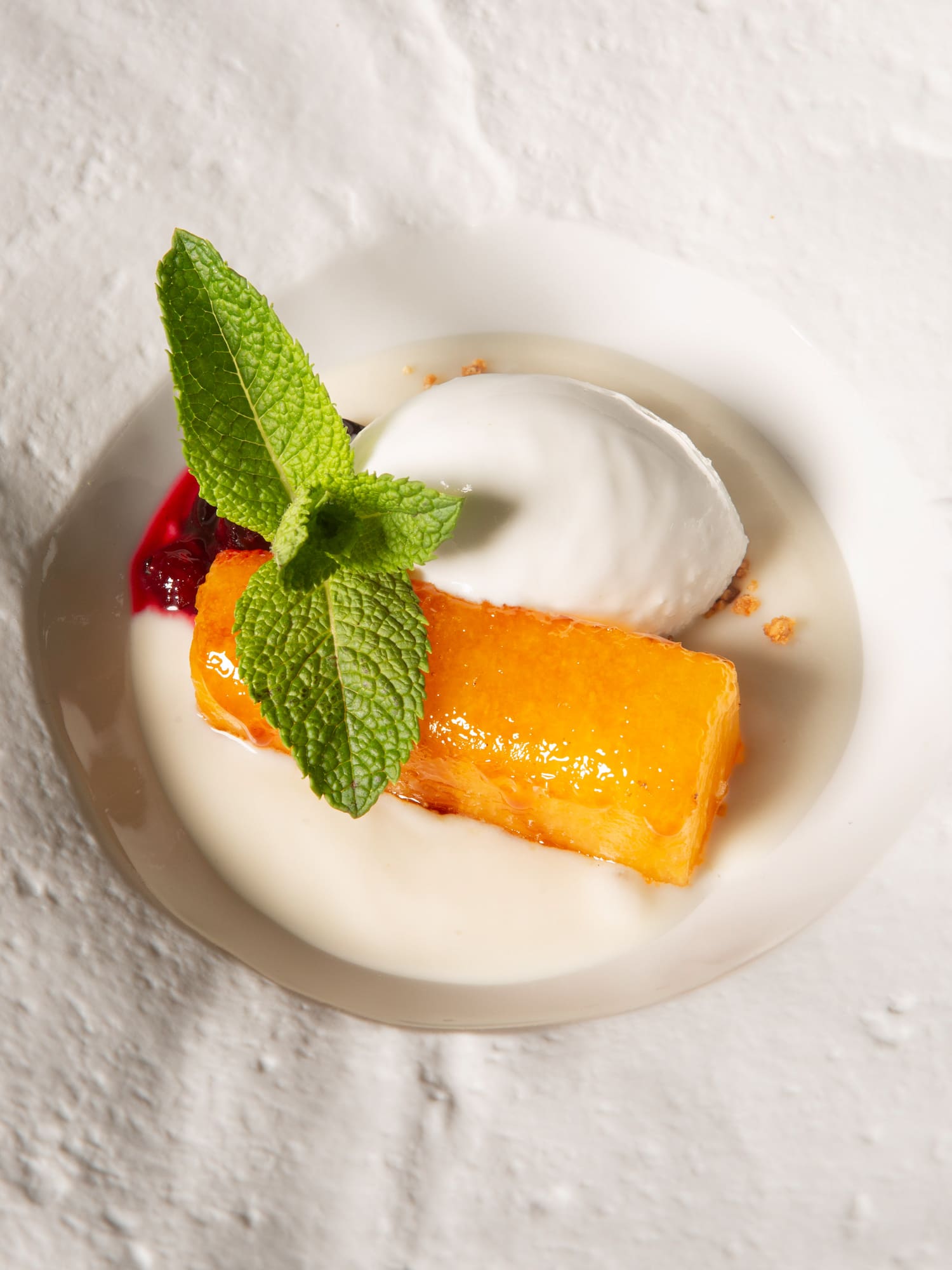 Glazed orange cake with white ice cream, fresh mint, and berry sauce.