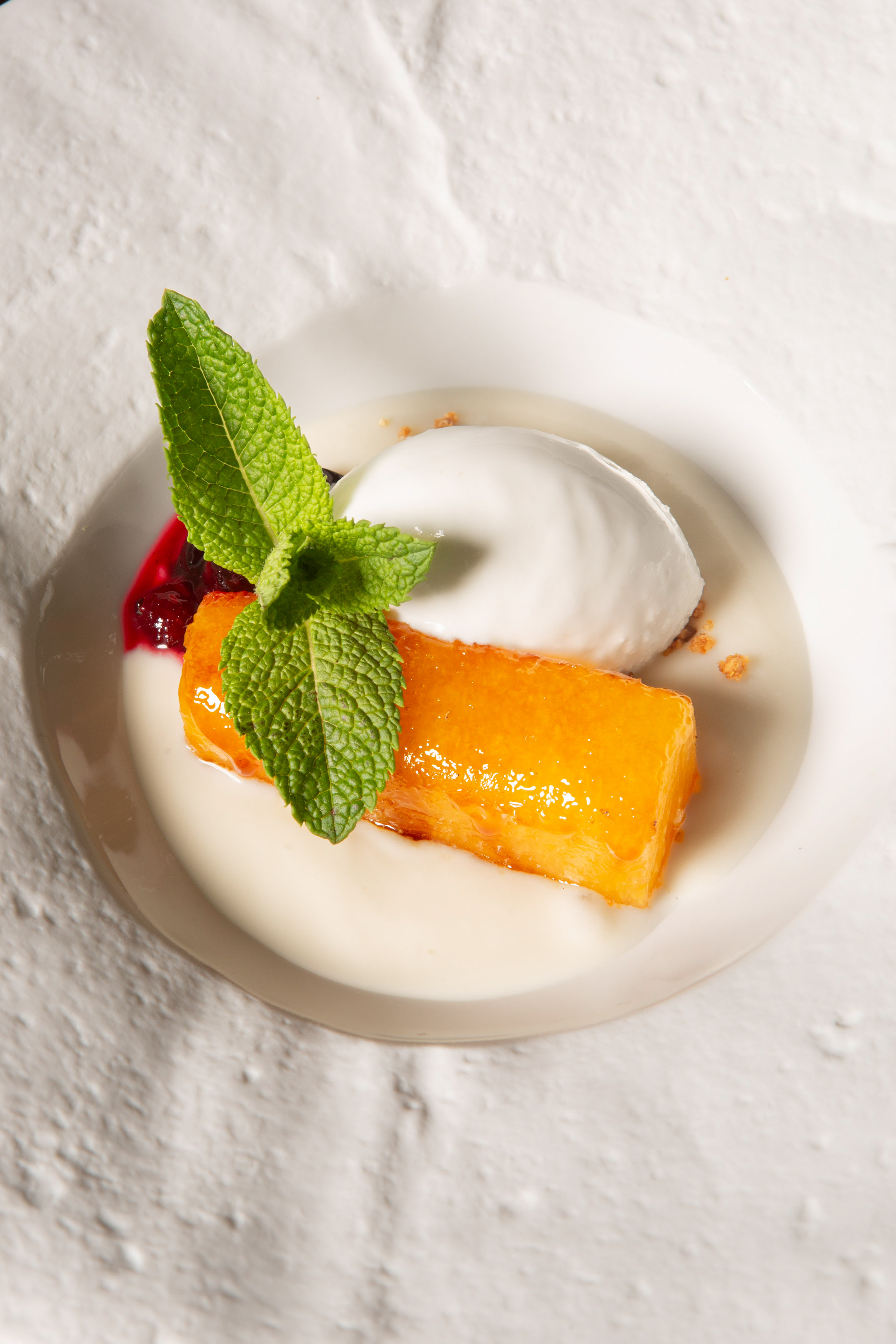Glazed orange cake with white ice cream, fresh mint, and berry sauce.