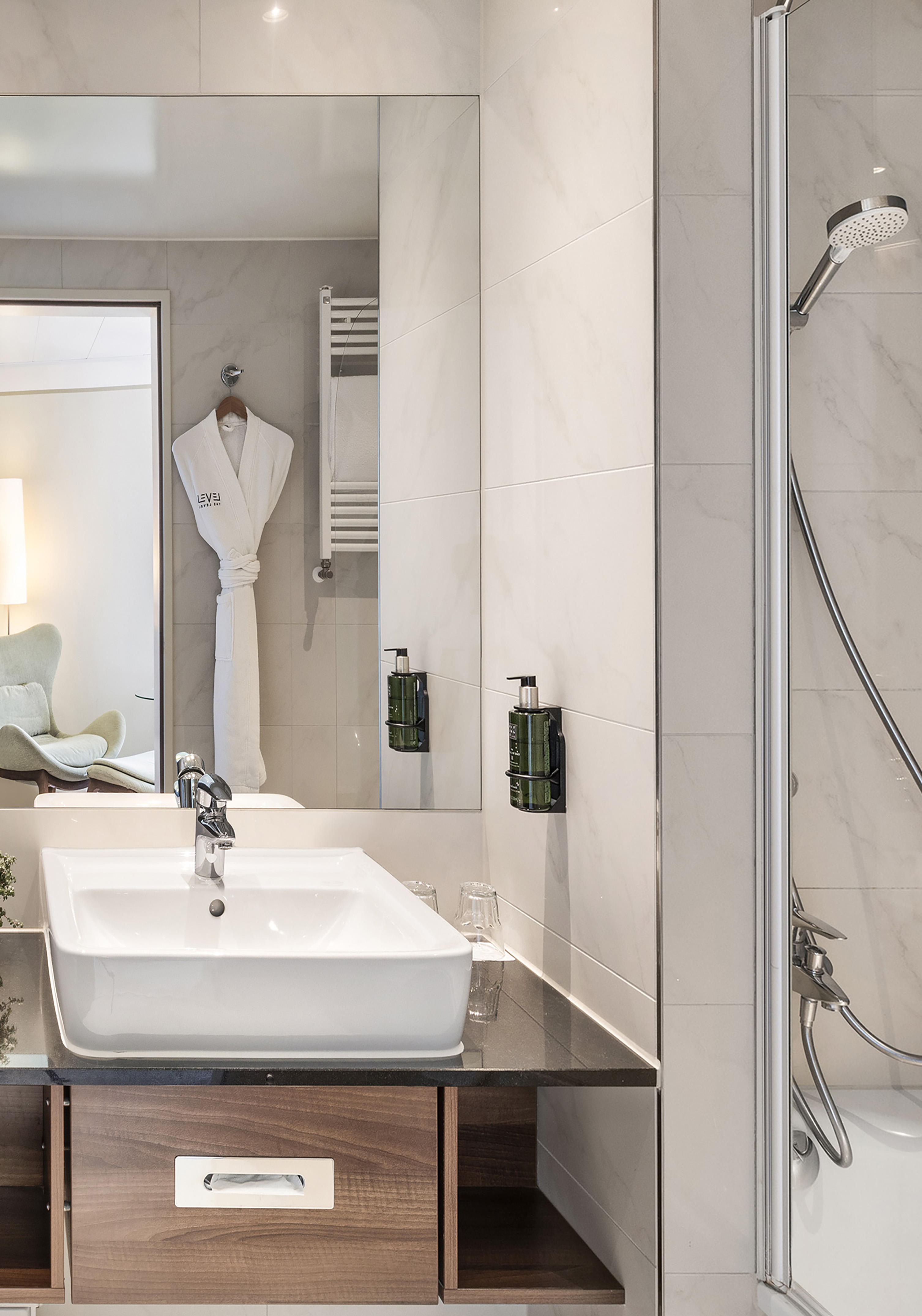 Modern hotel bathroom with sink, mirror reflecting robe, shower, marble walls.