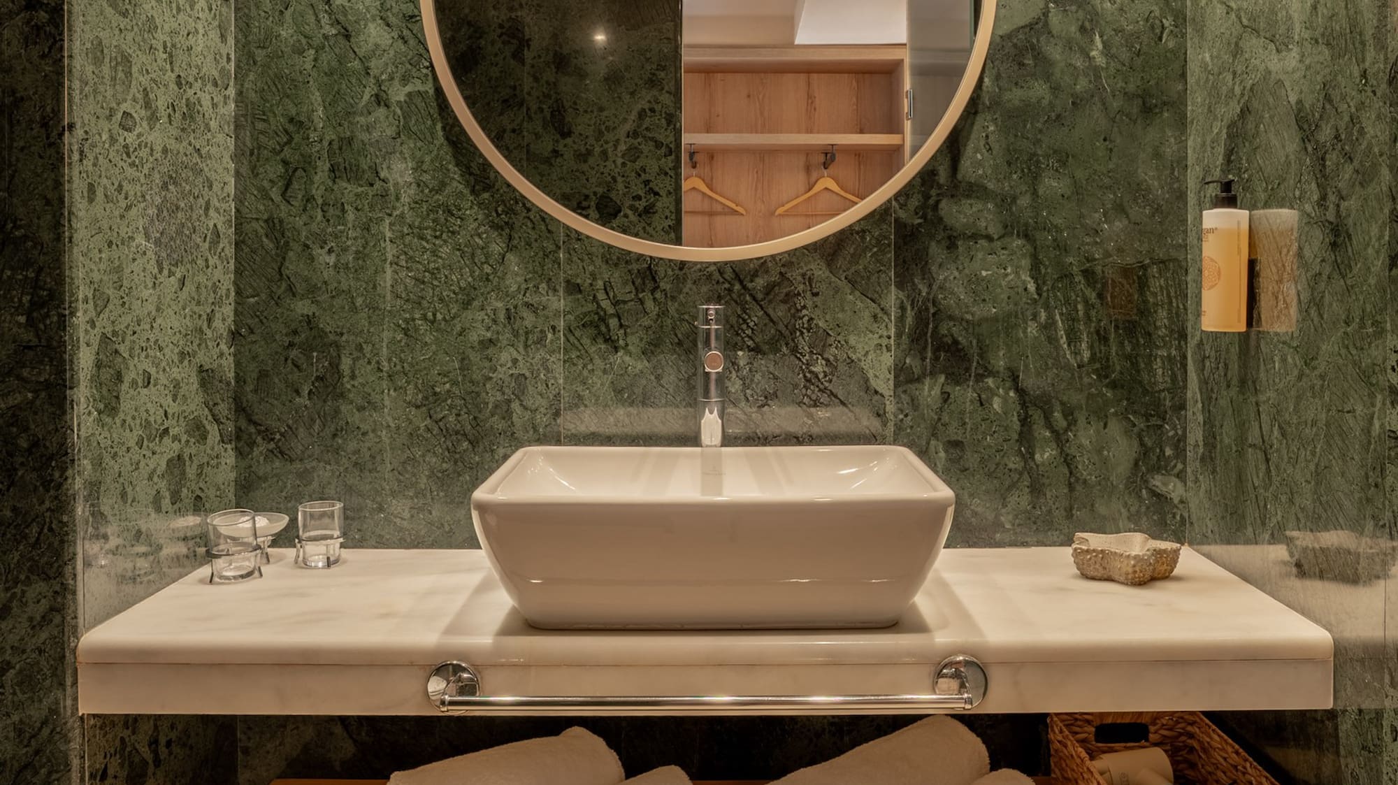 Modern bathroom with green marble, vessel sink, round mirror, and wood storage bench.