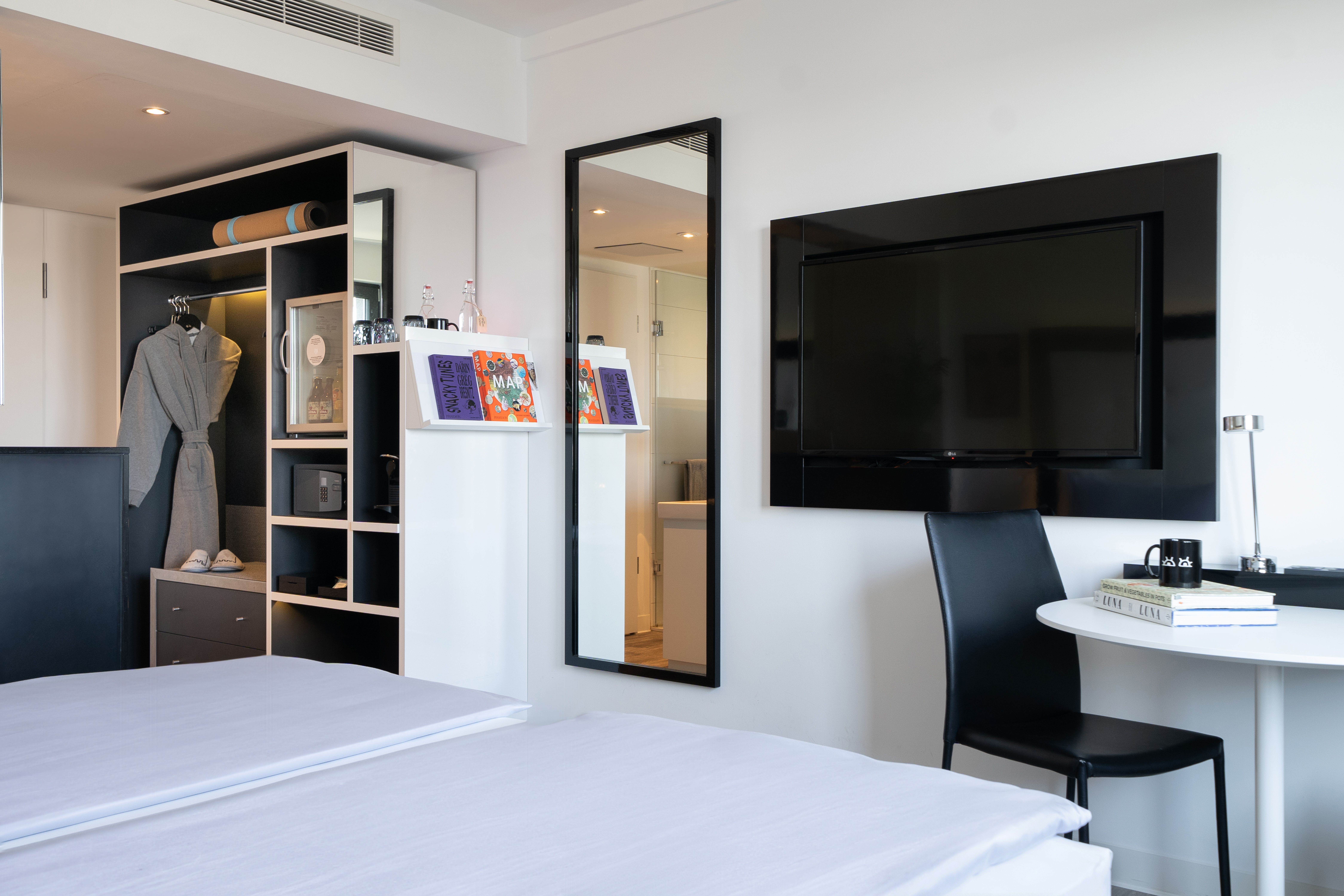 Modern hotel room with white bed, open closet, TV, and workspace.