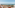 Sunny balcony overlooking ocean and sandy beach, with two lounge chairs.