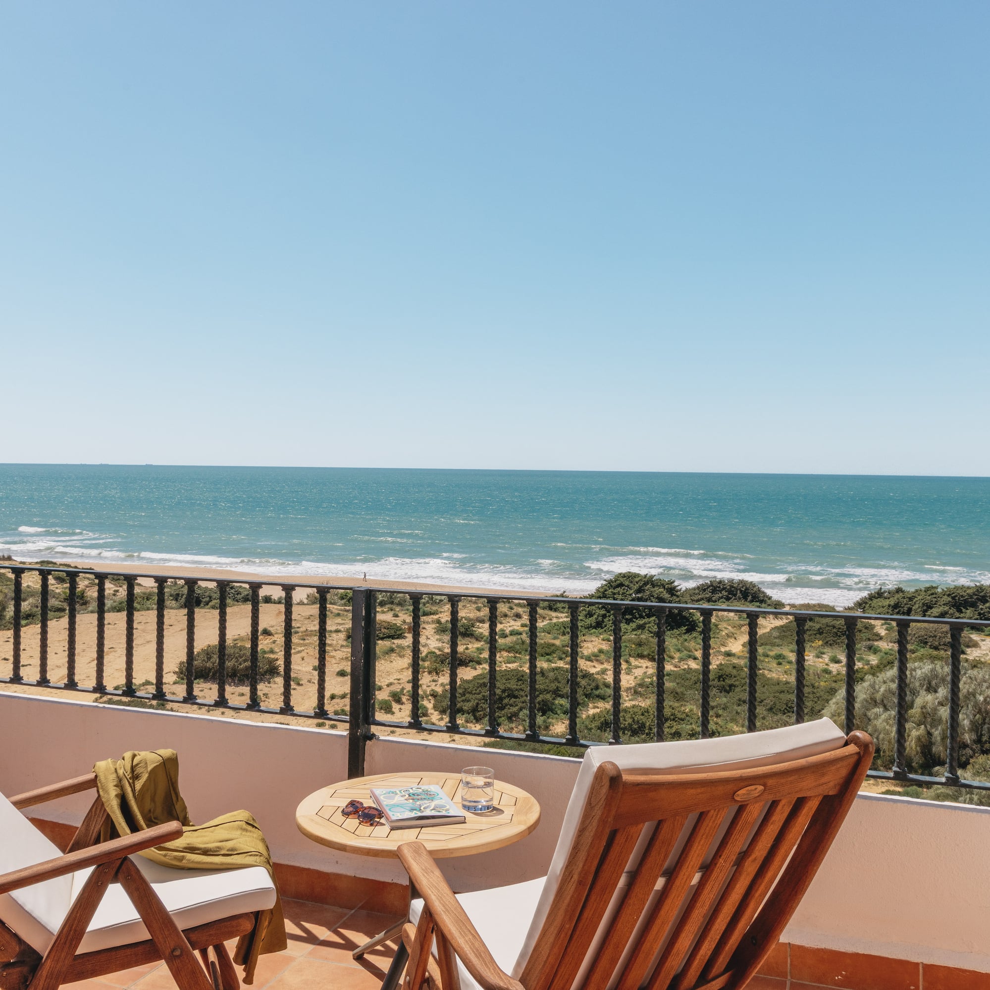 Sunny balcony overlooking ocean and sandy beach, with two lounge chairs.