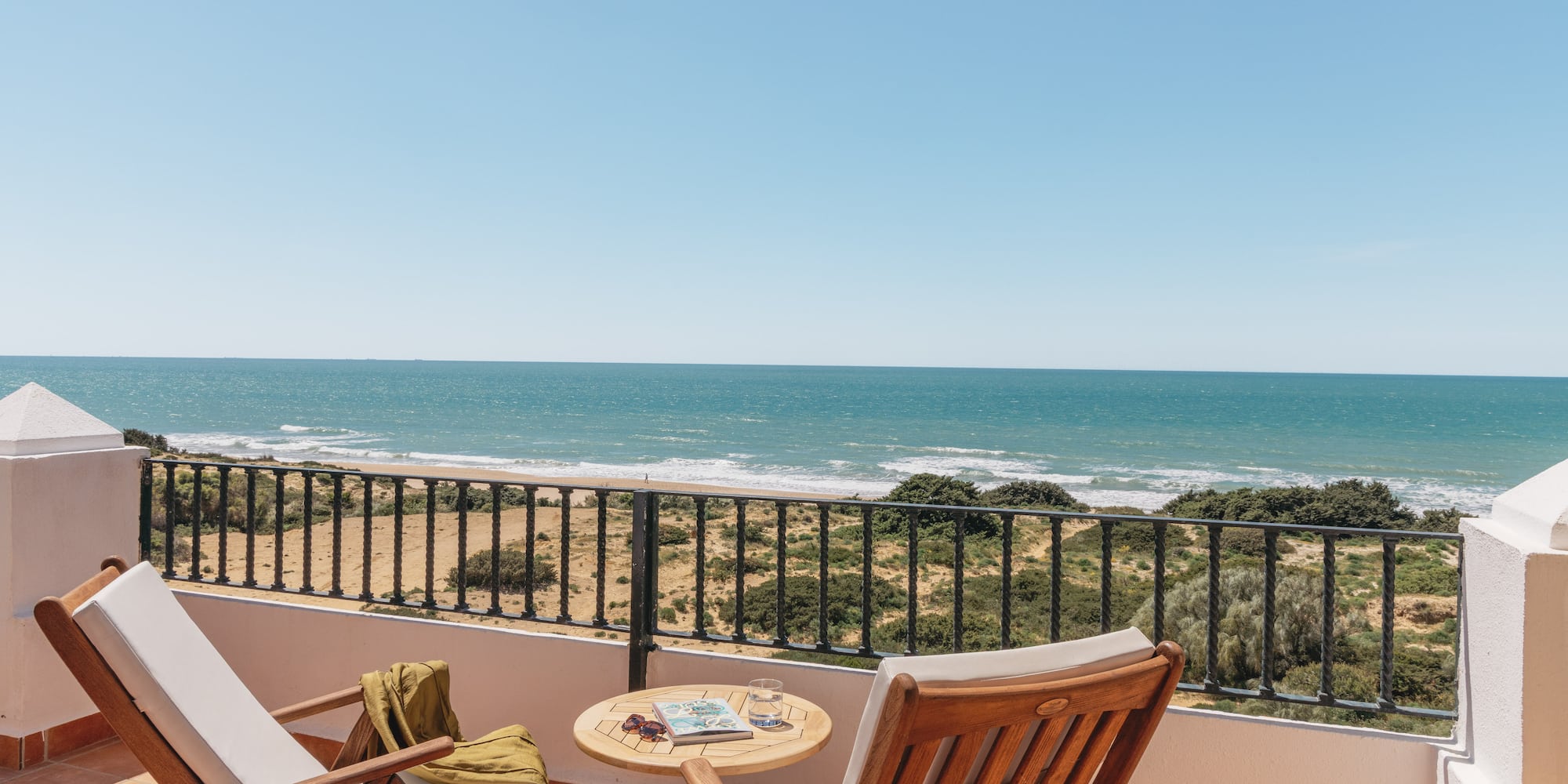 Sunny balcony overlooking ocean and sandy beach, with two lounge chairs.