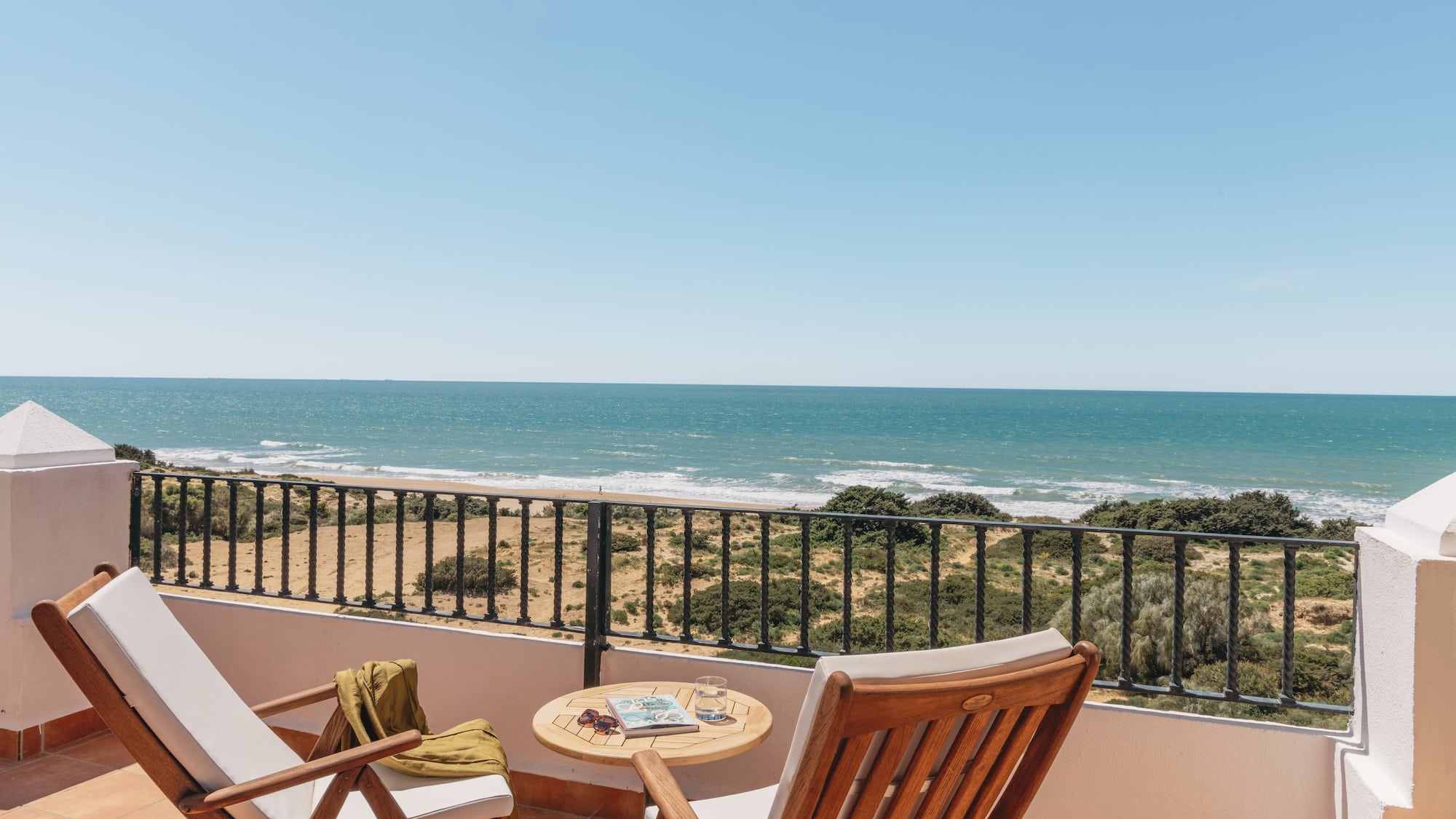 Sunny balcony overlooking ocean and sandy beach, with two lounge chairs.