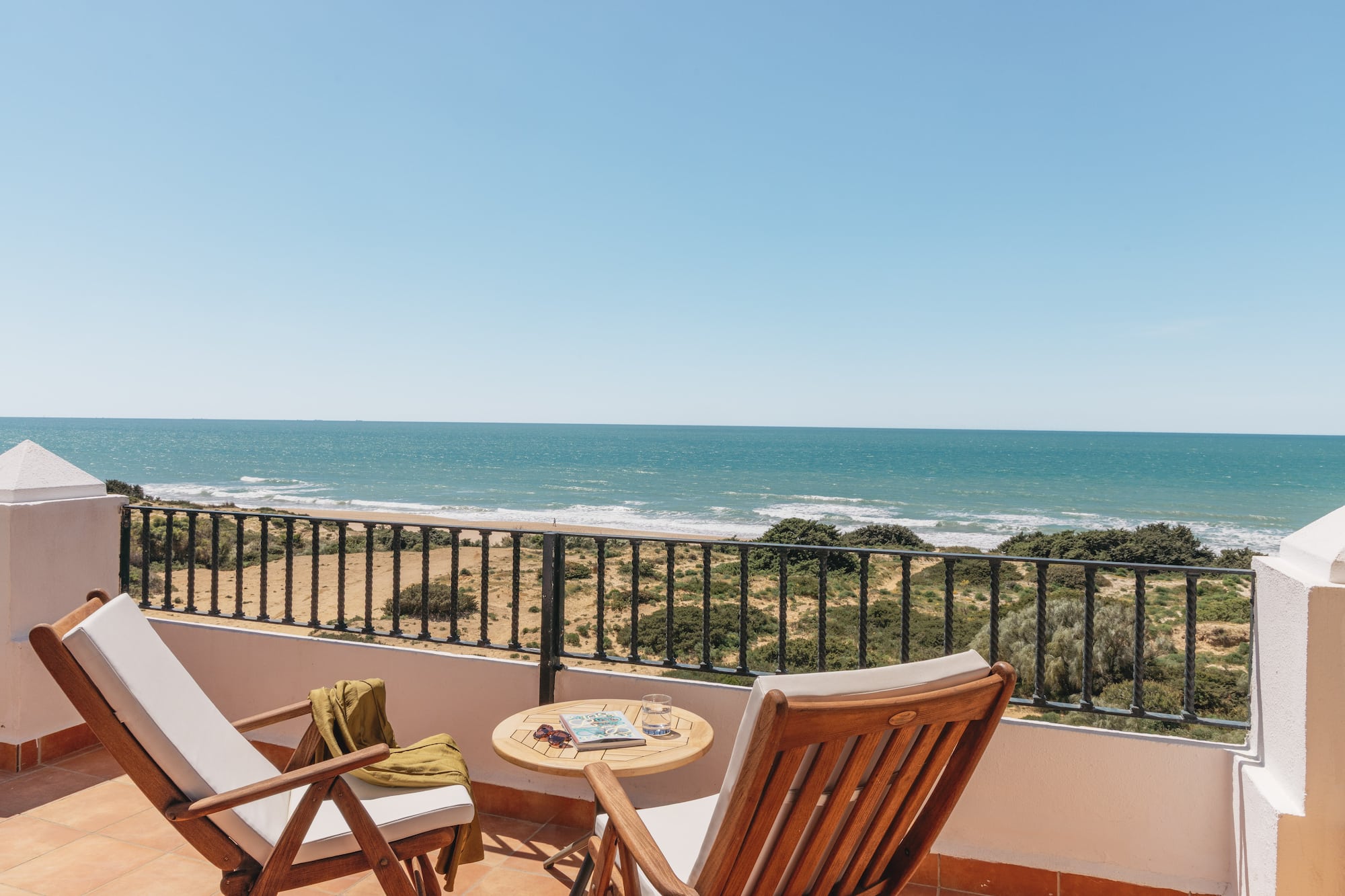 Sunny balcony overlooking ocean and sandy beach, with two lounge chairs.