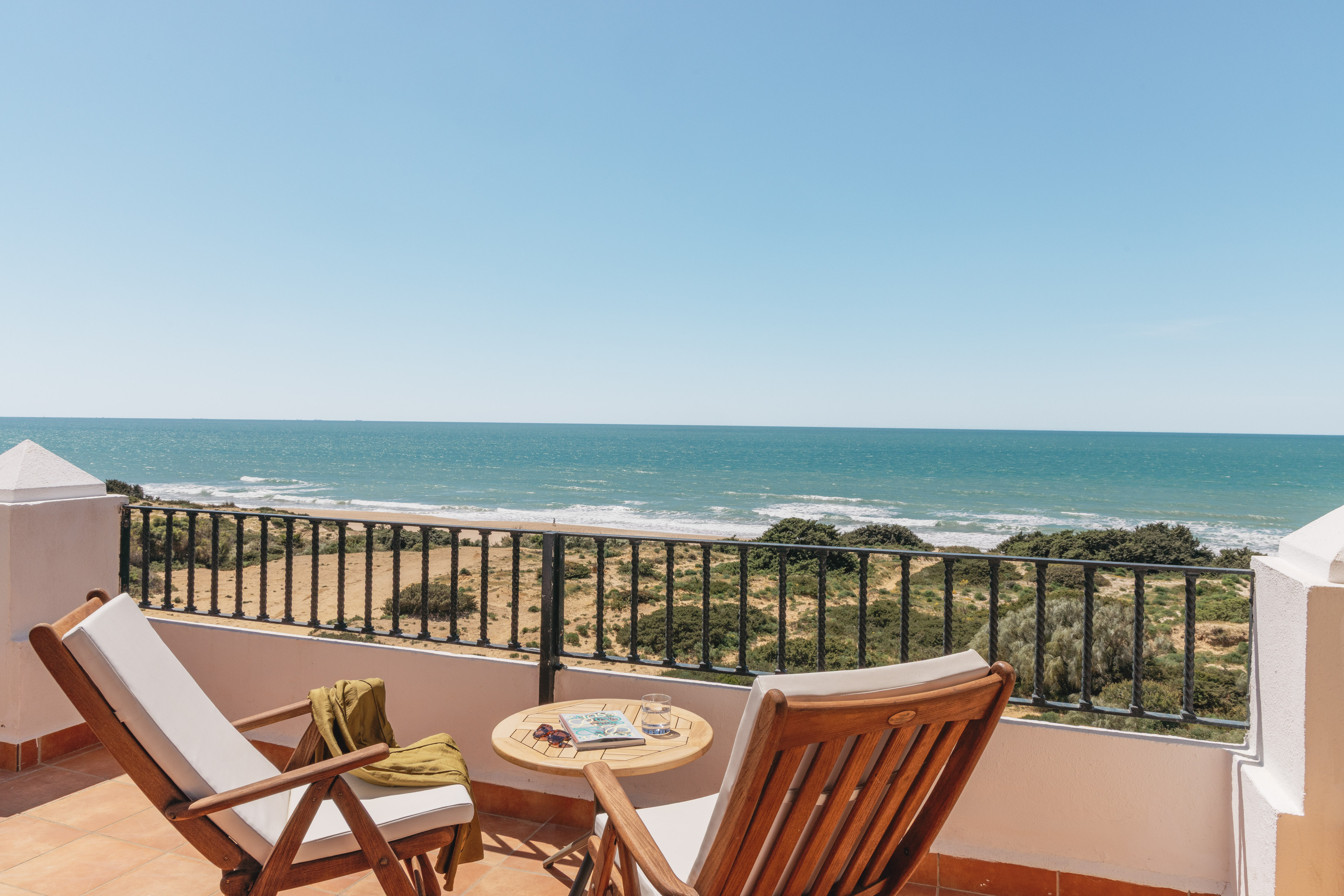 Sunny balcony overlooking ocean and sandy beach, with two lounge chairs.