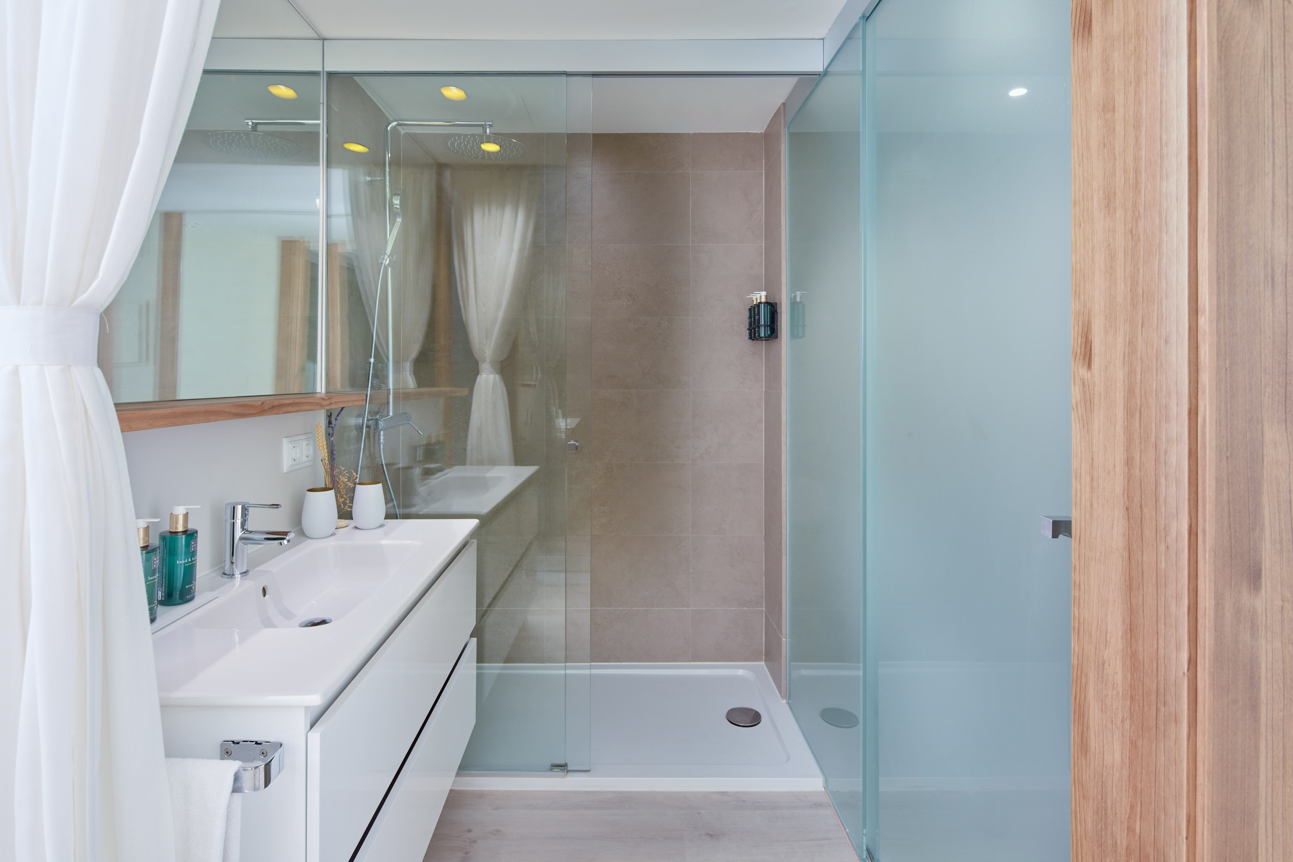 Modern bathroom with white vanity, glass shower, rain shower, and wood details.
