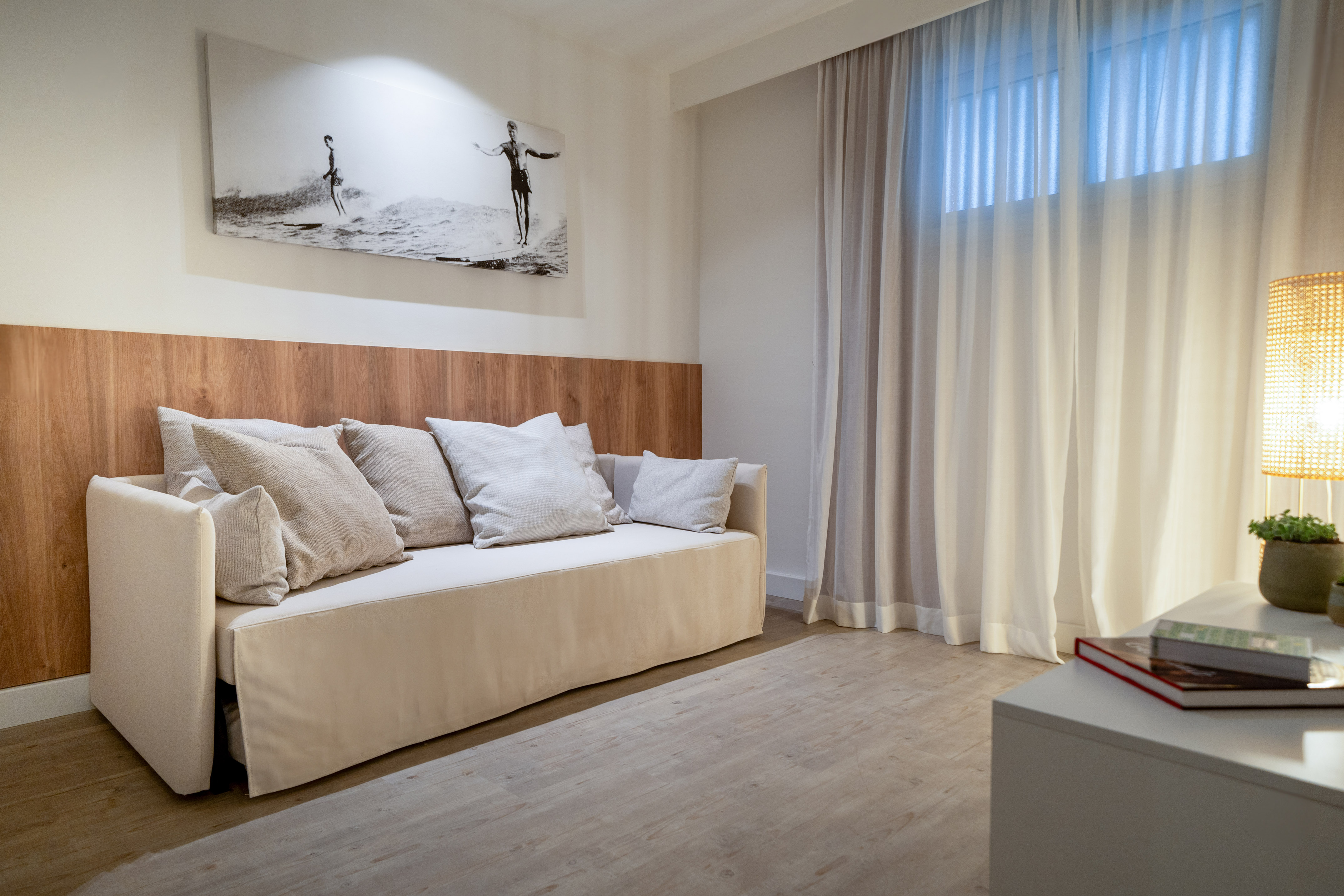 Modern hotel room with daybed, wood headboard, surfing art, sheer curtains.