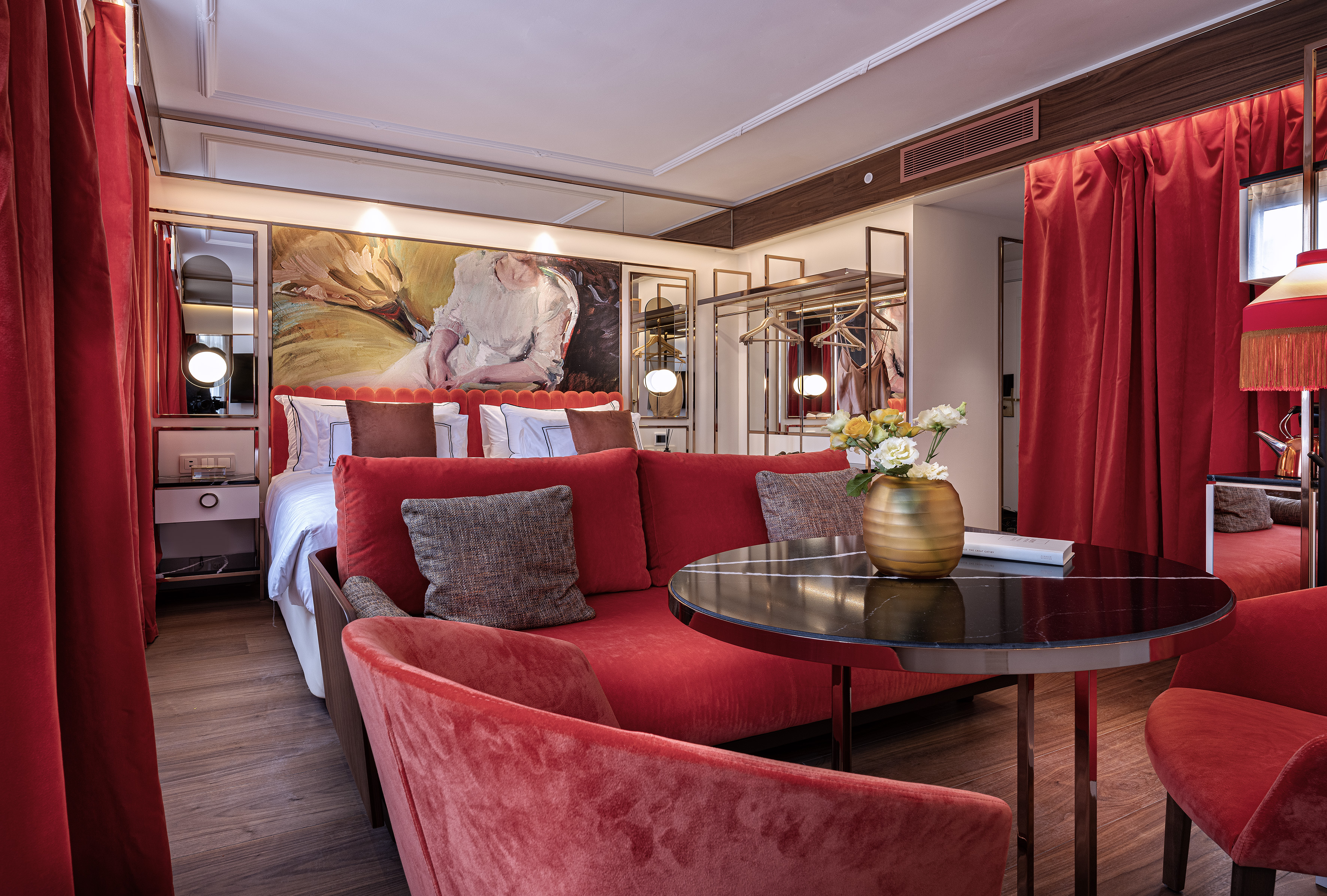 Luxury hotel suite: red velvet sofa, bed, artwork, modern design.