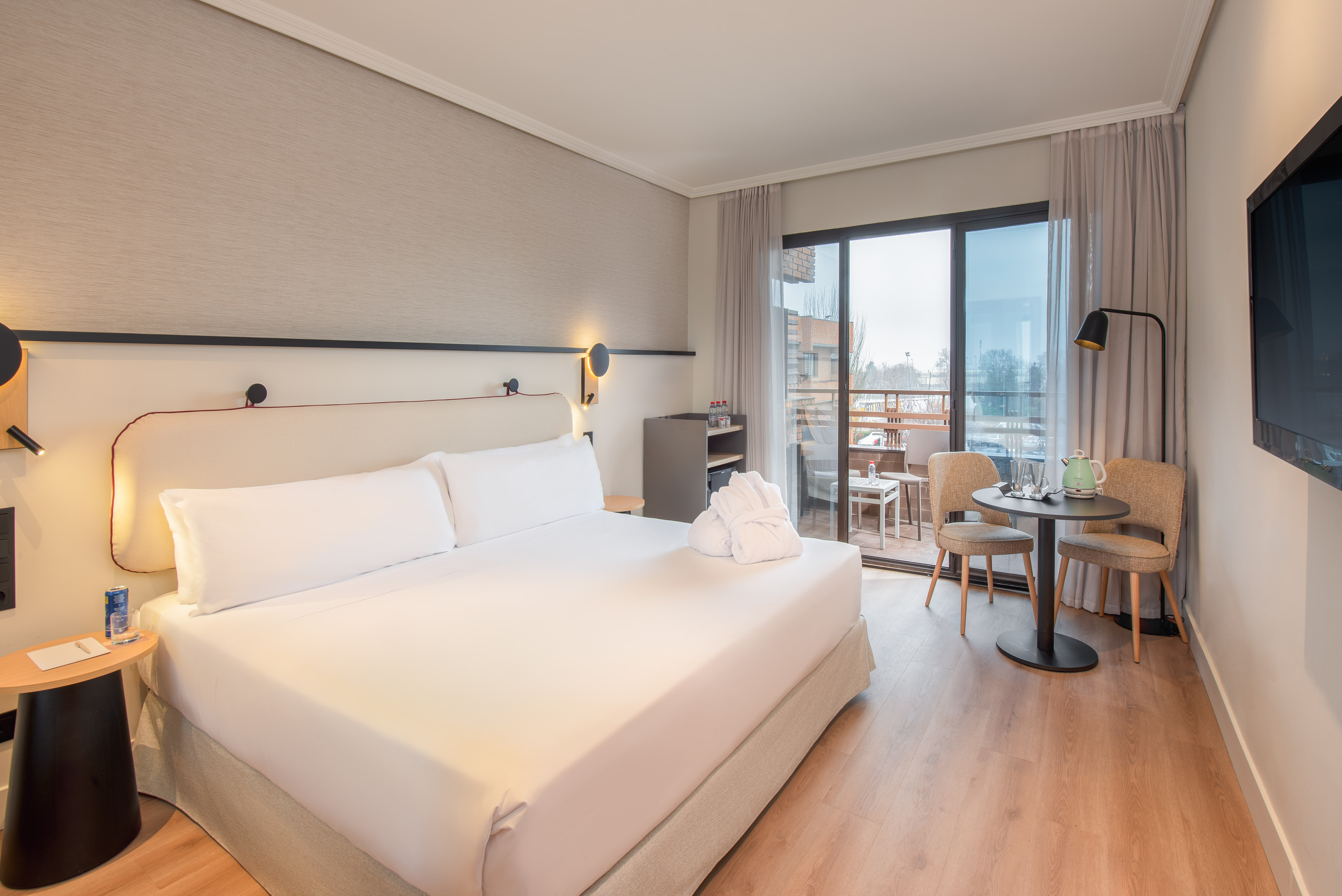 Modern hotel room with double bed, private balcony, and cozy seating area.