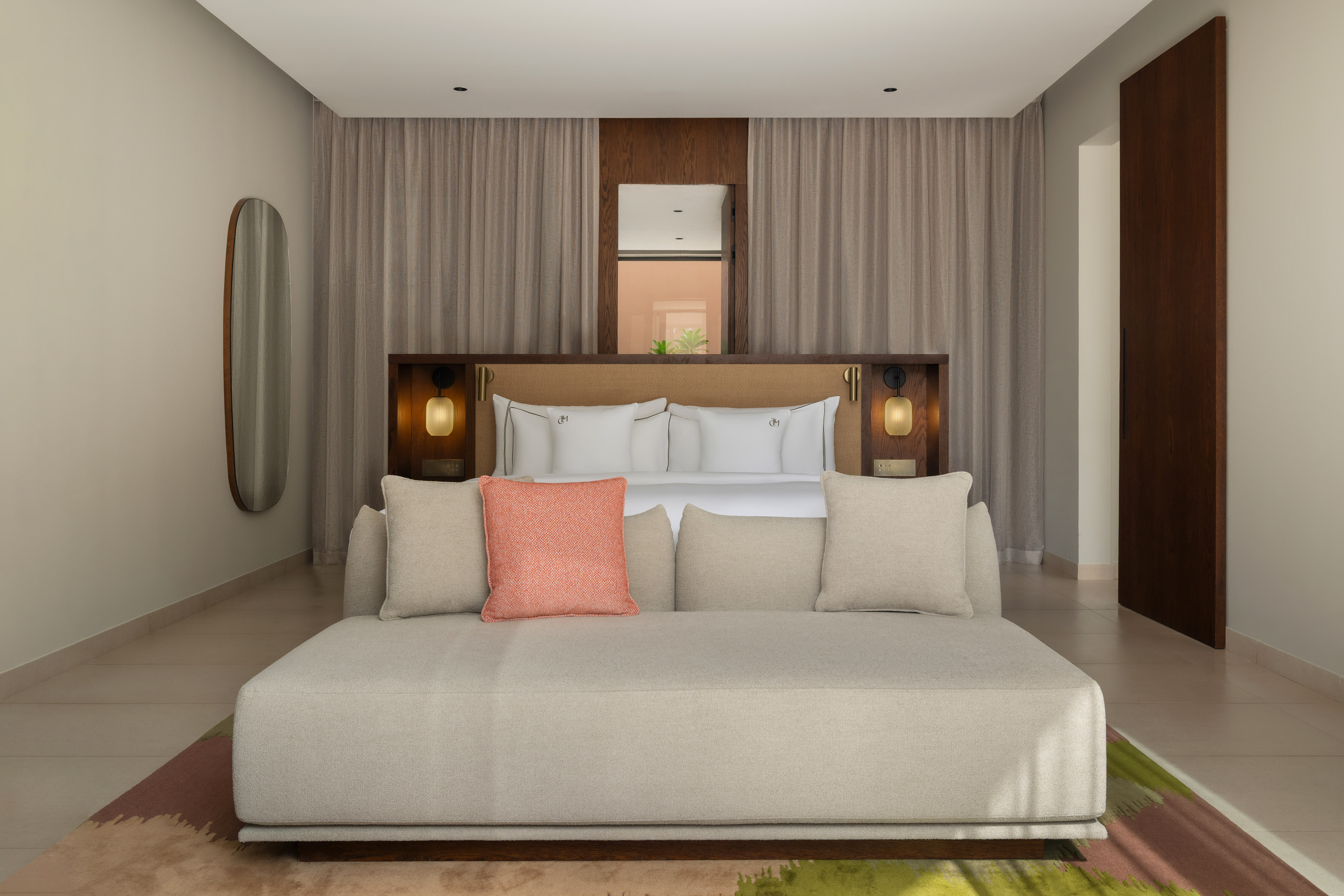 Modern hotel bedroom with a large bed, beige sofa, and wall lamps.