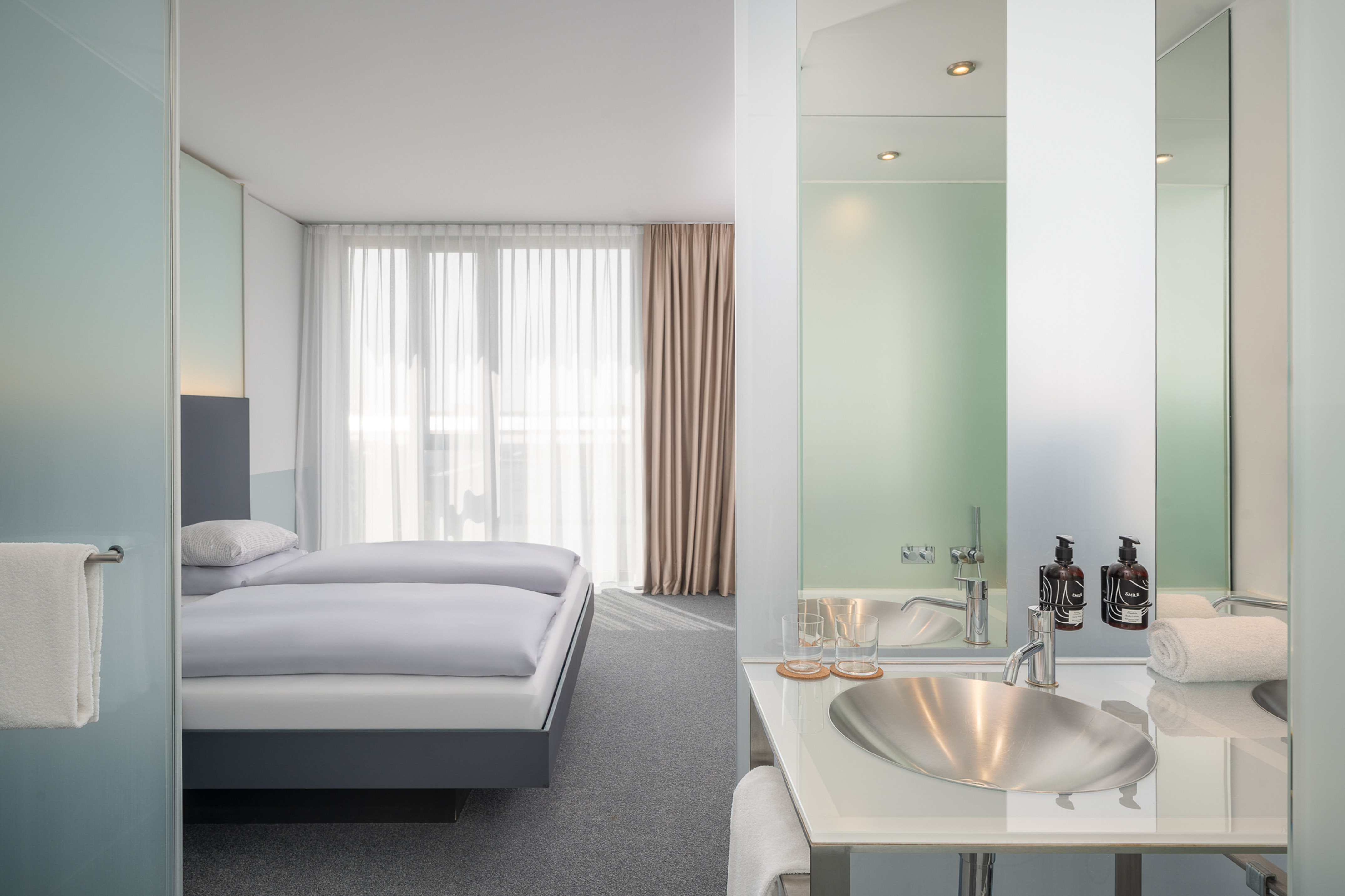 Bright, modern hotel room with twin beds, large window, and sleek vanity sink.