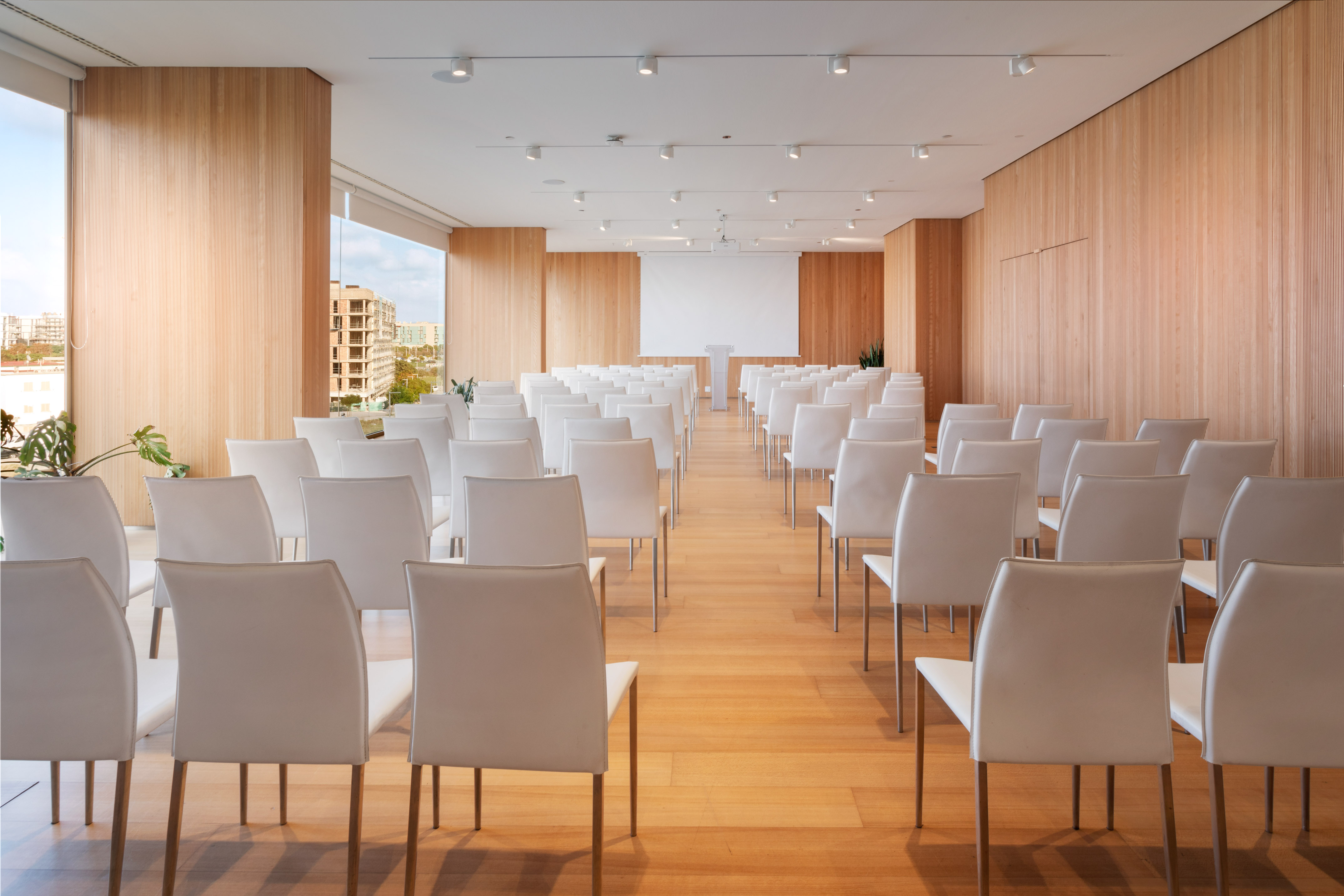 Modern conference room with white chairs, wood walls, projector, natural light.