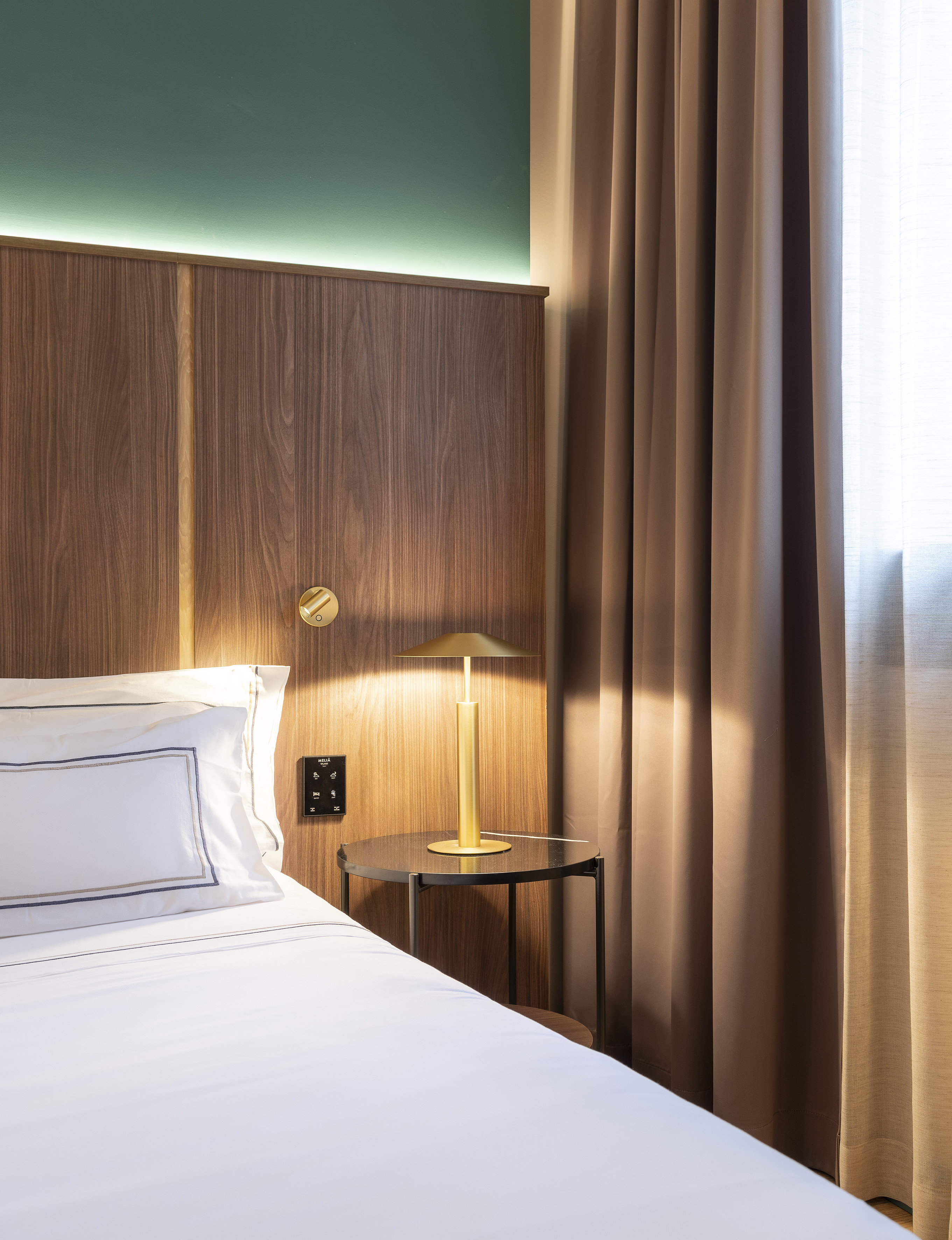 Hotel room with wooden headboard, green ambient light, white bed, and gold lamp.