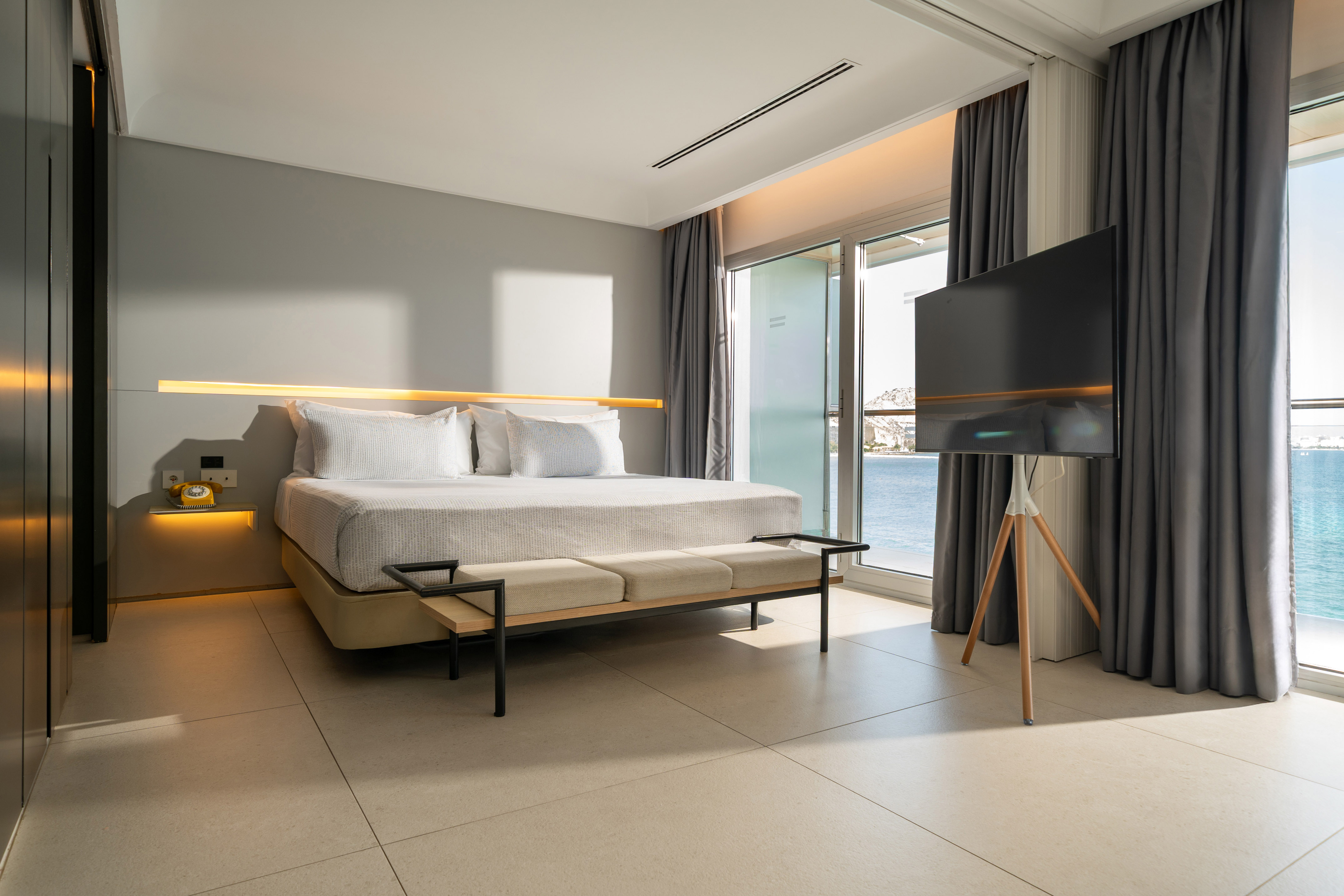 Modern hotel bedroom with sea view, bed, TV, and contemporary design.