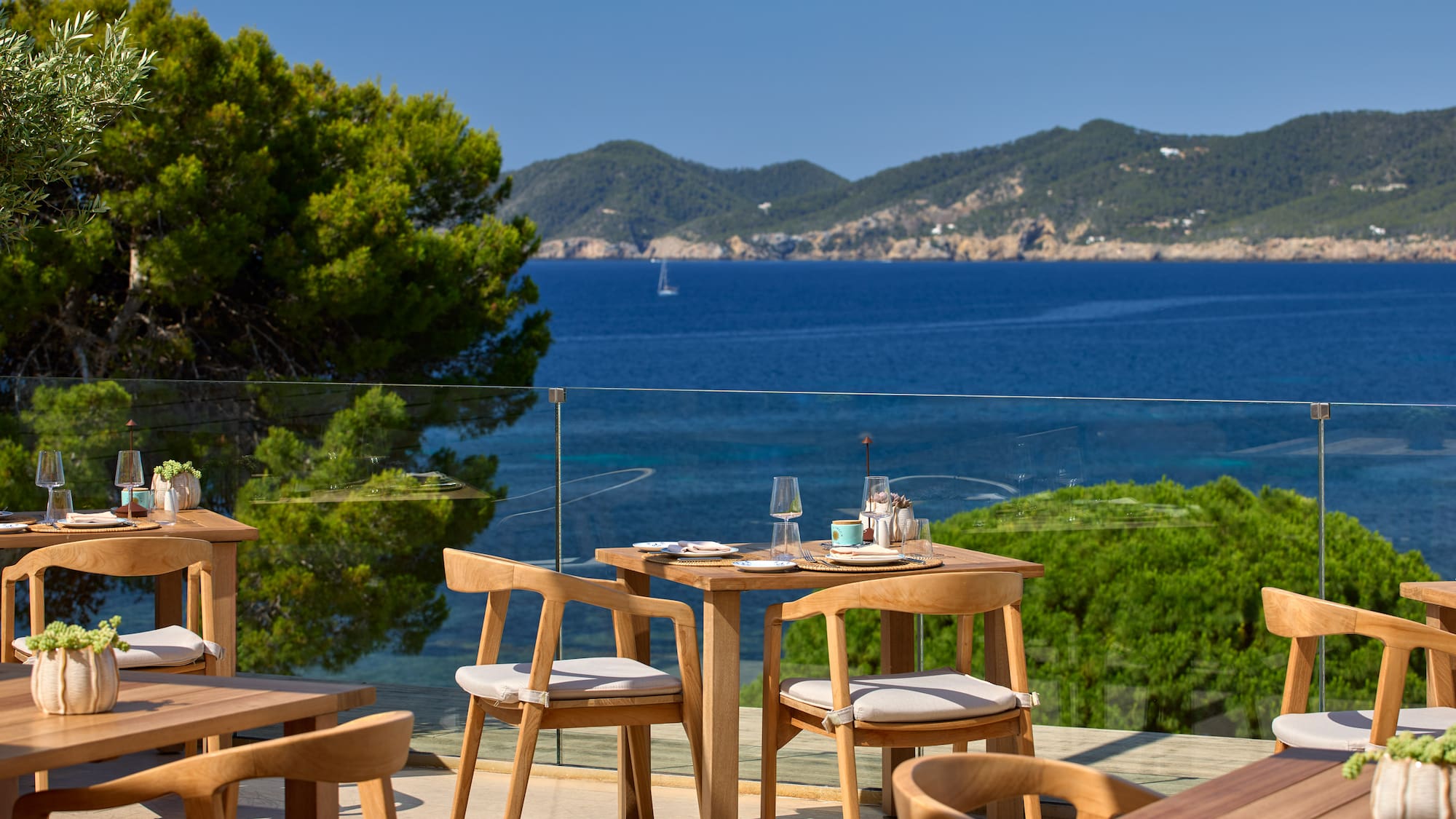 Outdoor restaurant terrace with sea views and wooden furniture.