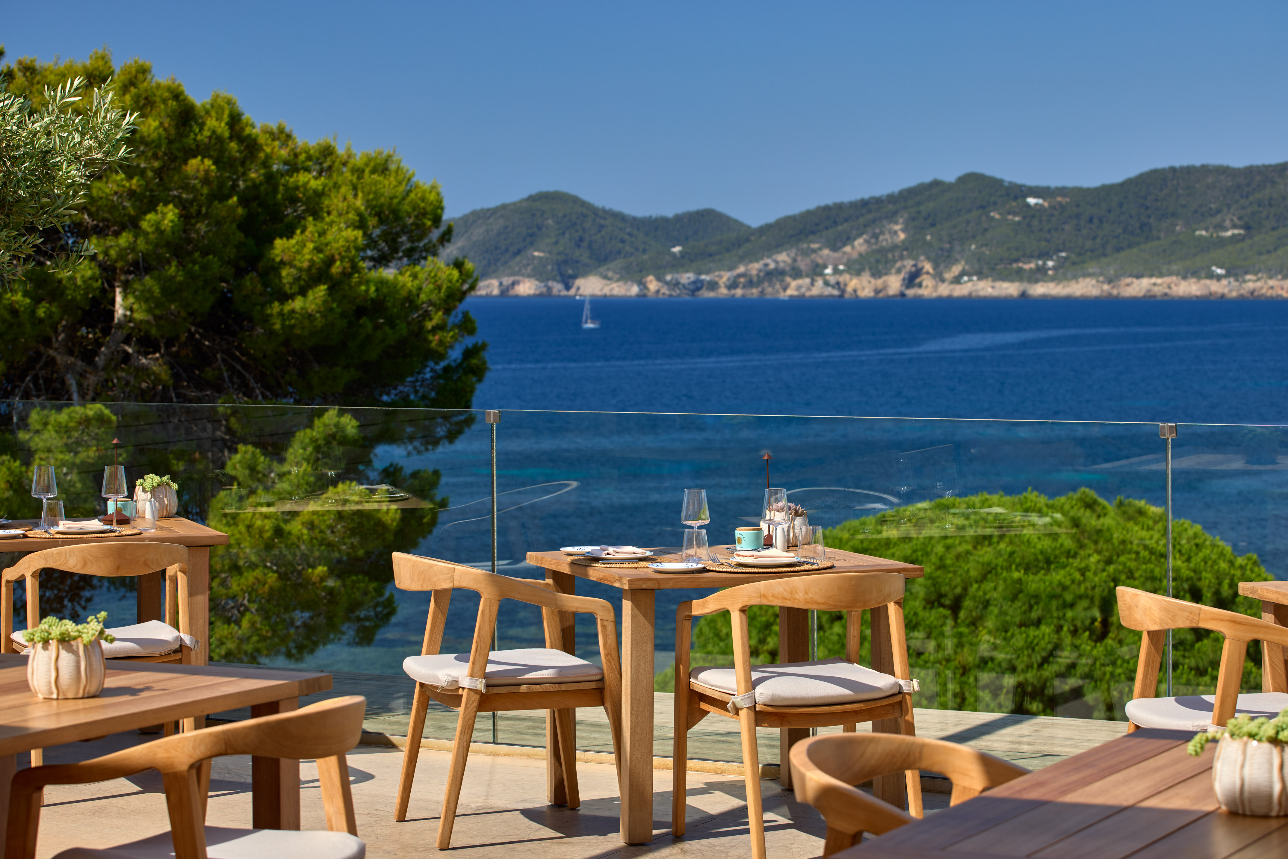 Outdoor restaurant terrace with sea views and wooden furniture.
