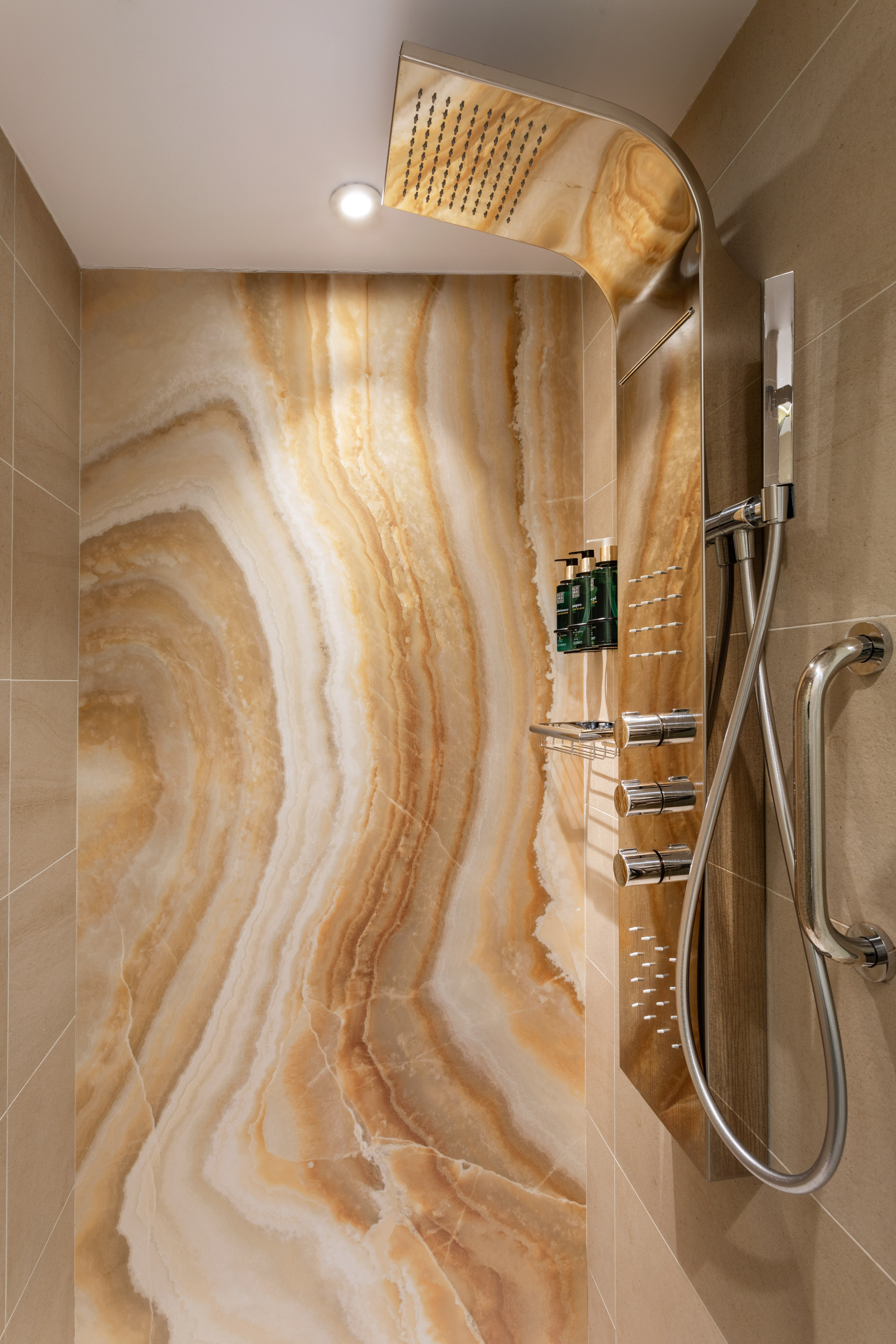 Modern shower with patterned onyx wall, chrome rain head, and grab bar.