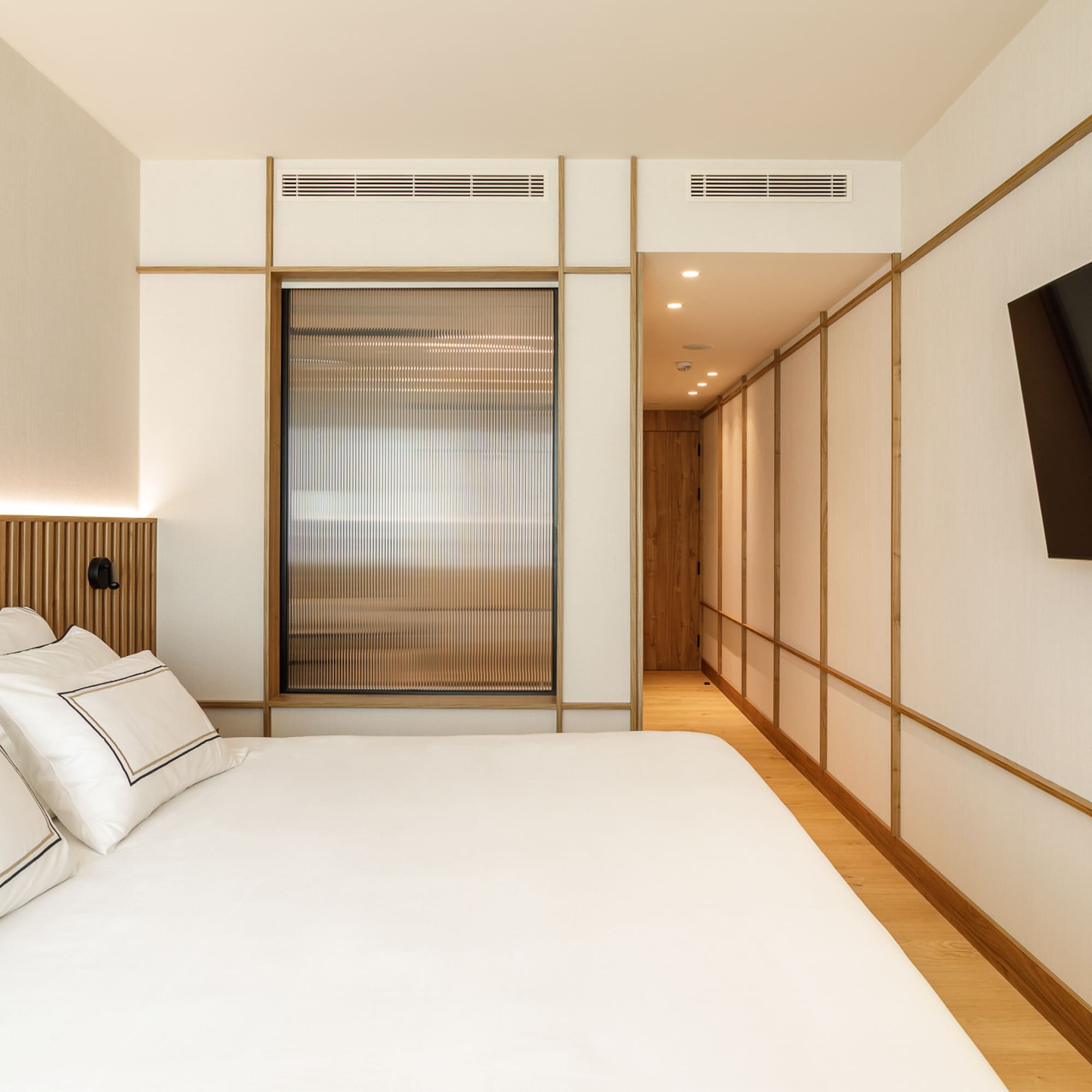 Modern minimalist bedroom with white bed, wooden accents, and wall-mounted TV.
