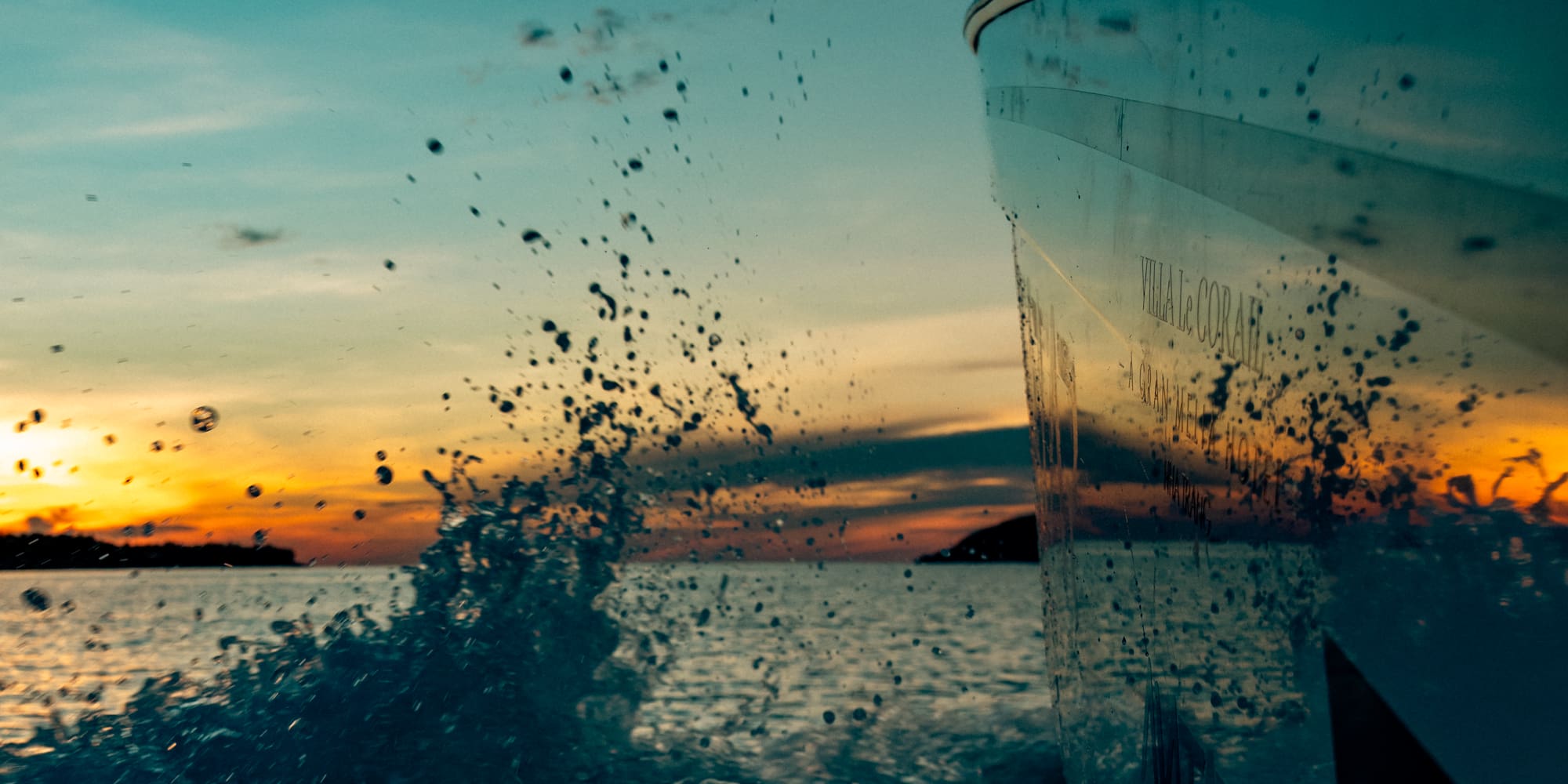 Proa de barco navegando al atardecer, salpicaduras de agua en el mar.