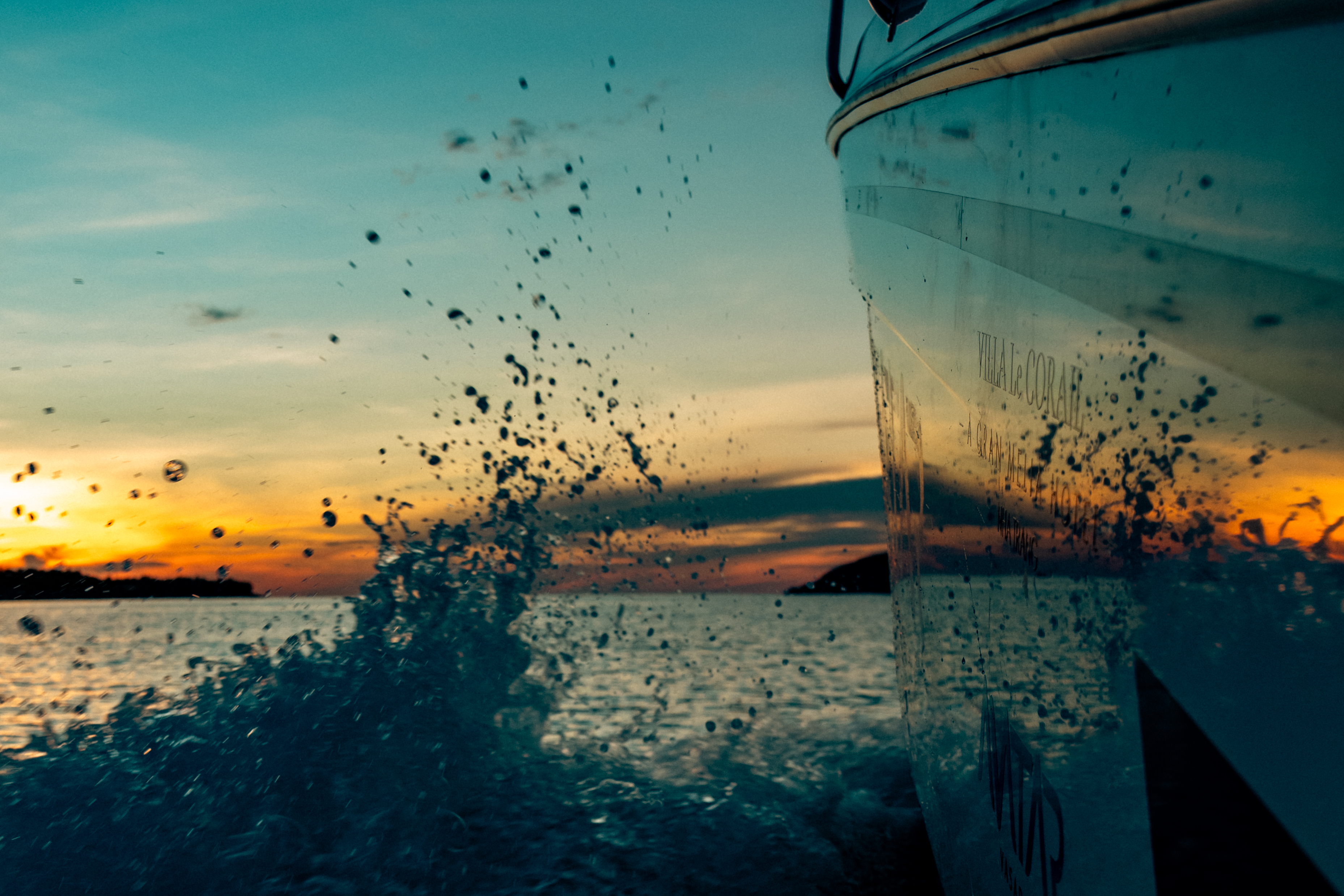 Proa de barco navegando al atardecer, salpicaduras de agua en el mar.