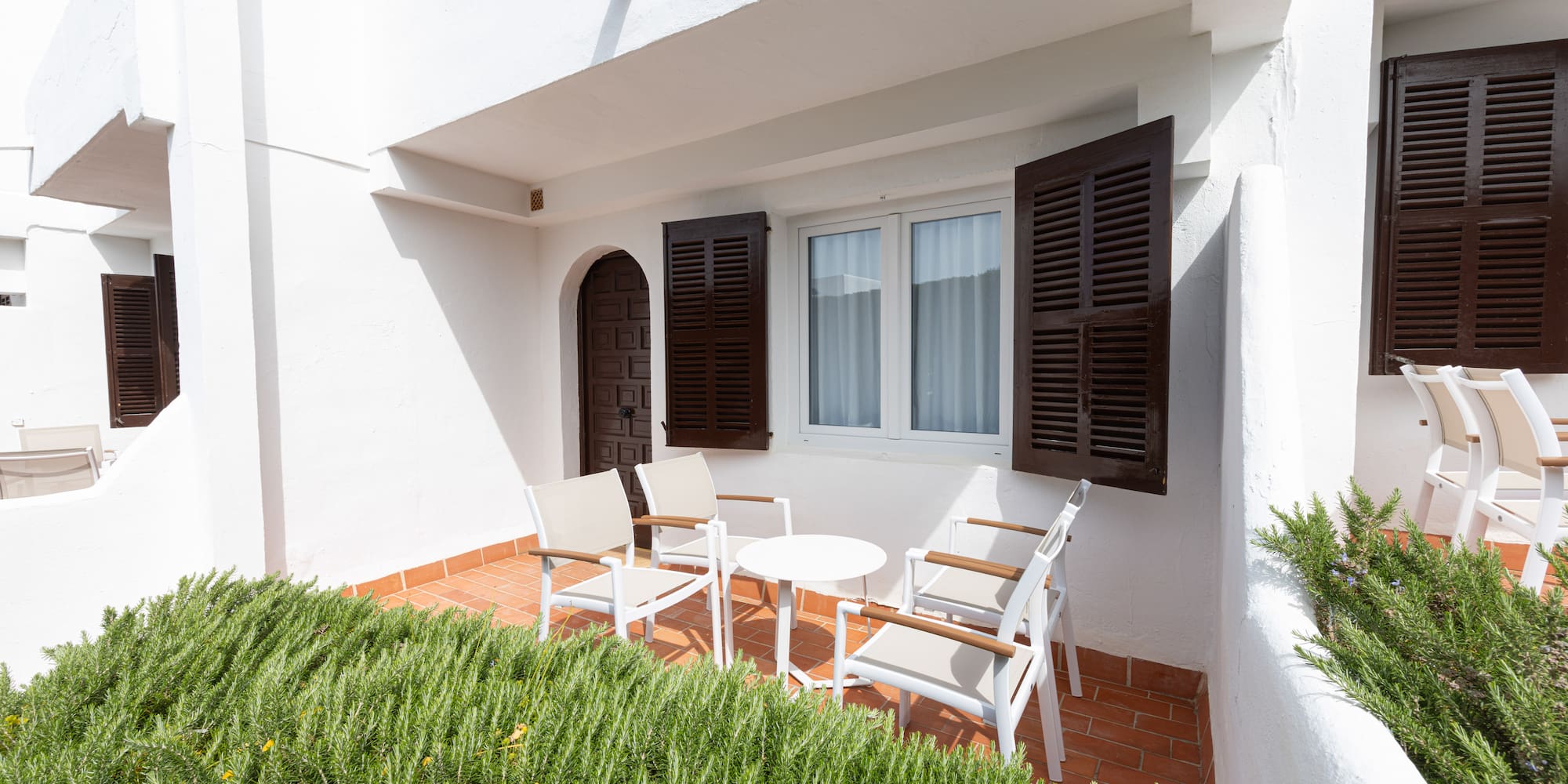White Mediterranean terrace with outdoor seating, brown shutters, and green rosemary.