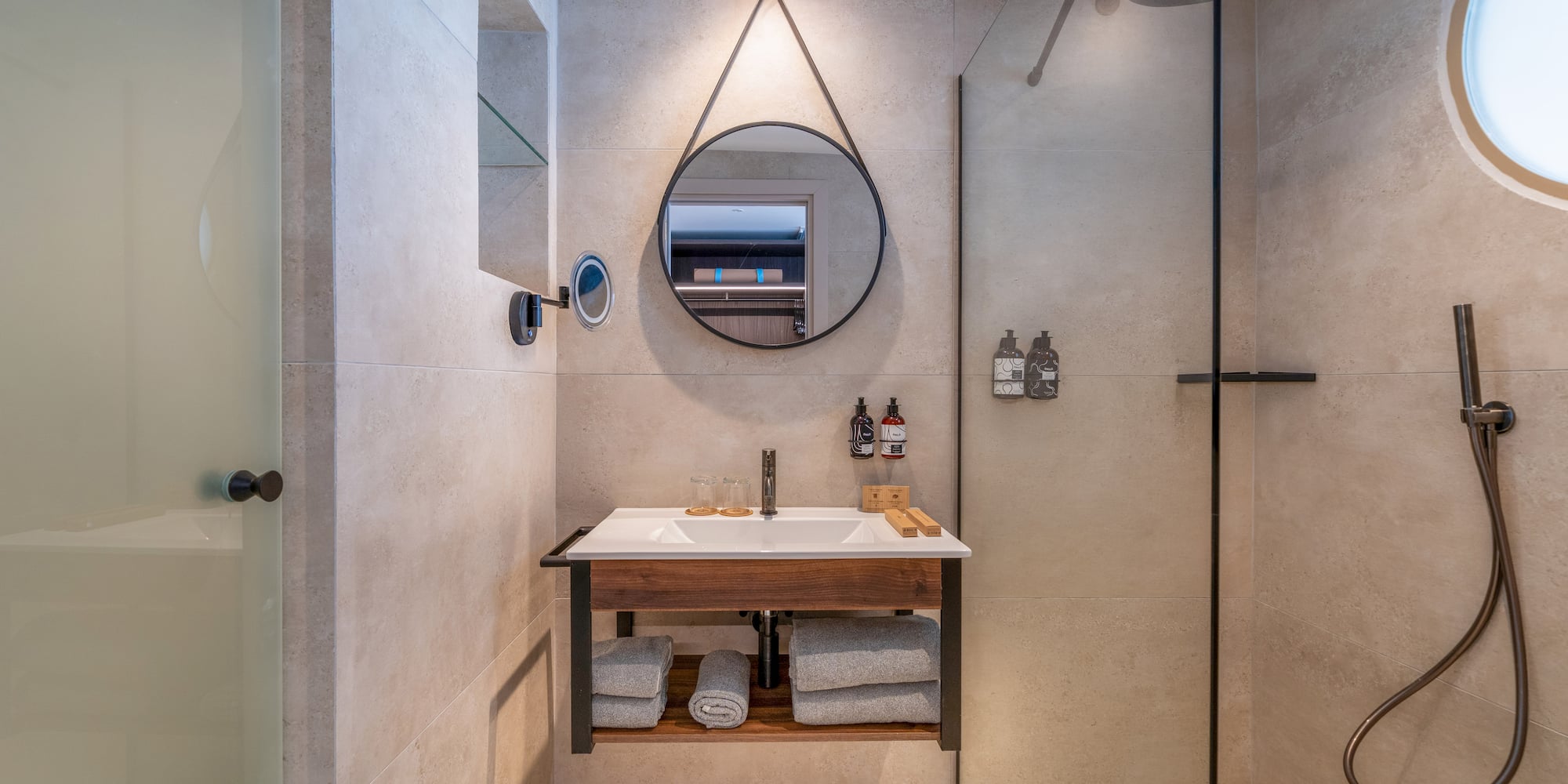 Modern bathroom with floating vanity, round mirror, and glass shower.