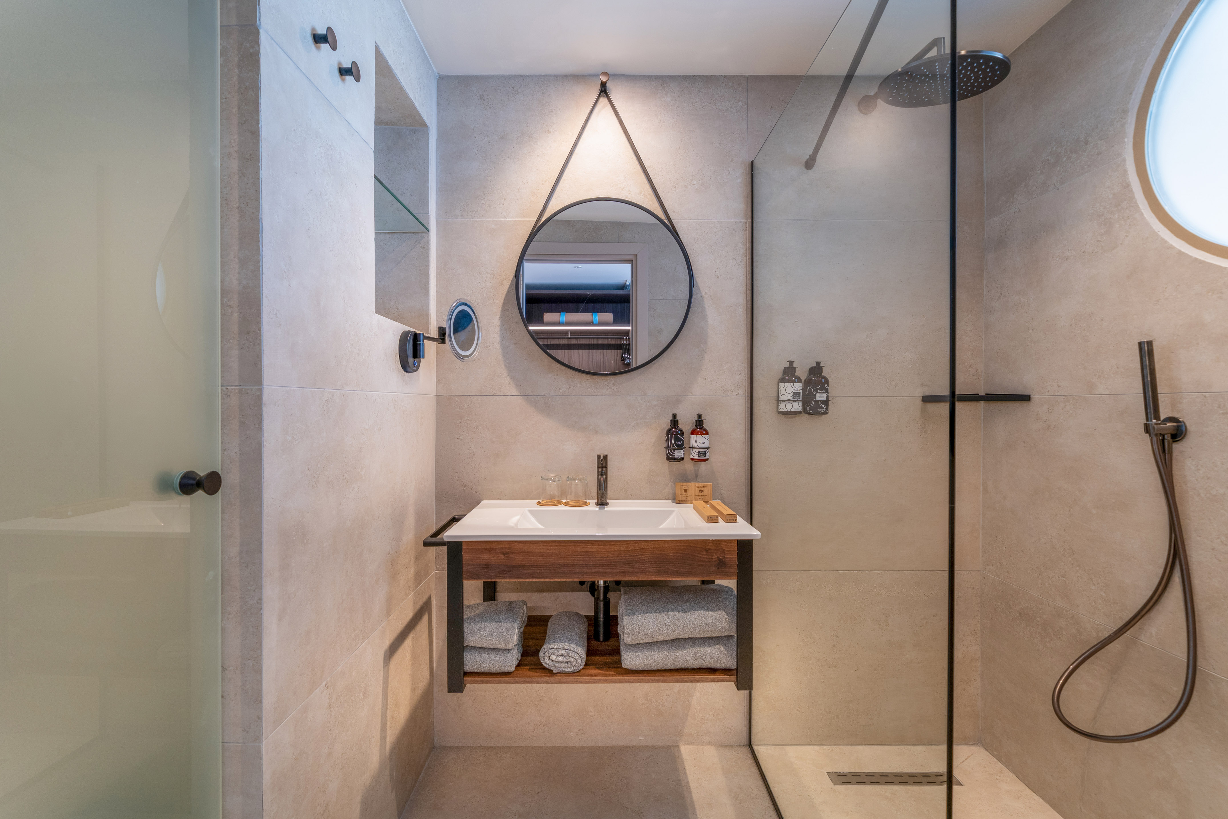 Modern bathroom with floating vanity, round mirror, and glass shower.