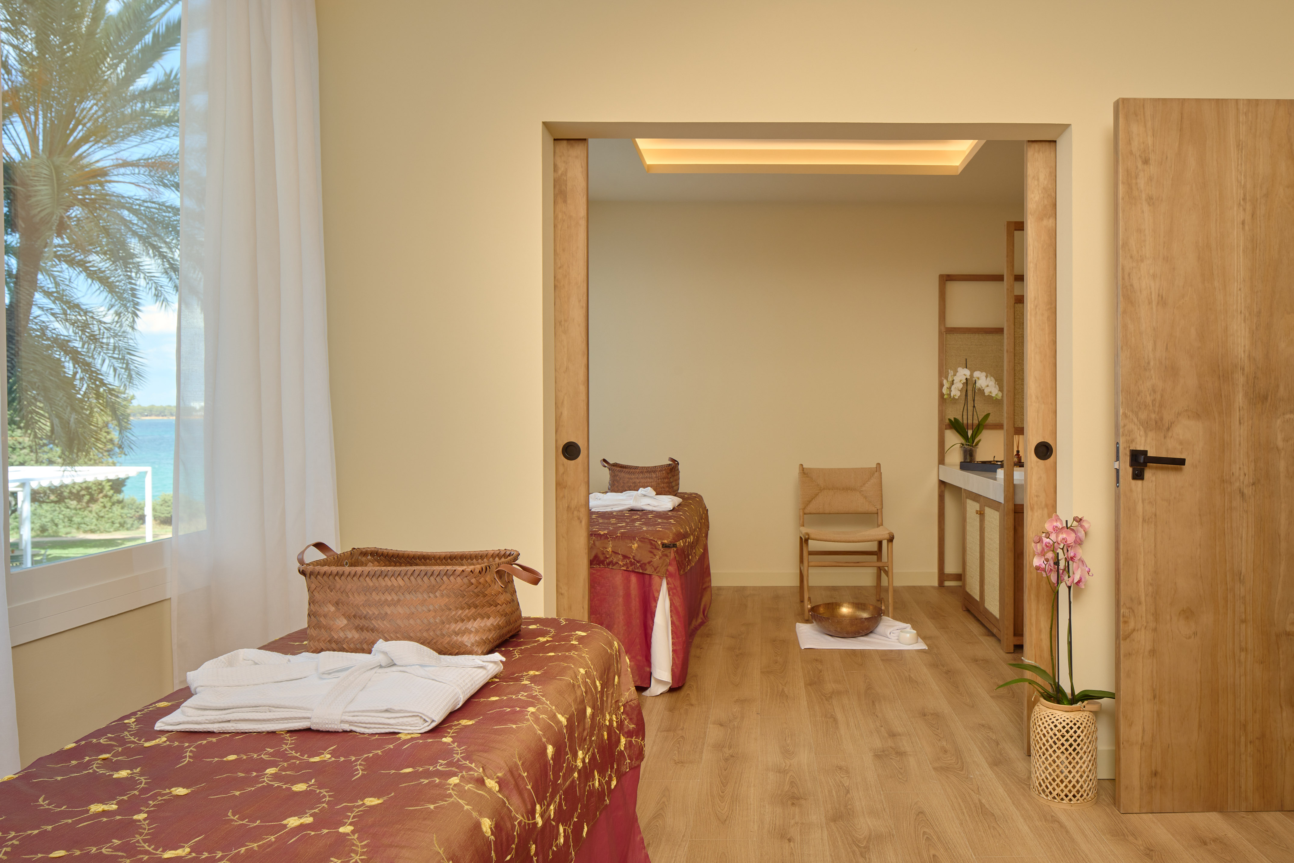 Tropical spa room with two massage tables, ocean view, and serene decor.