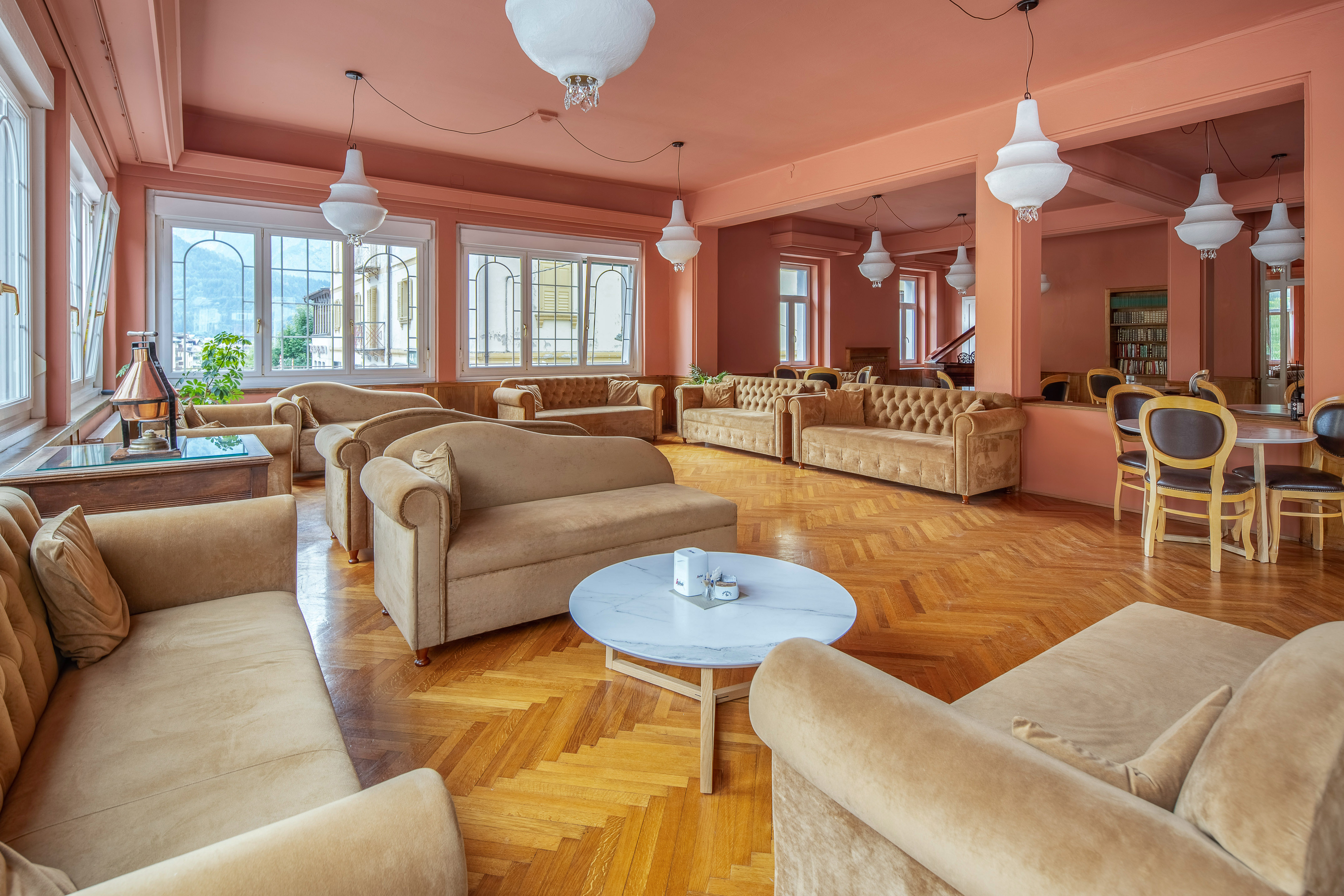 Peach hotel lounge, beige sofas, parquet floor, white lighting, large windows.