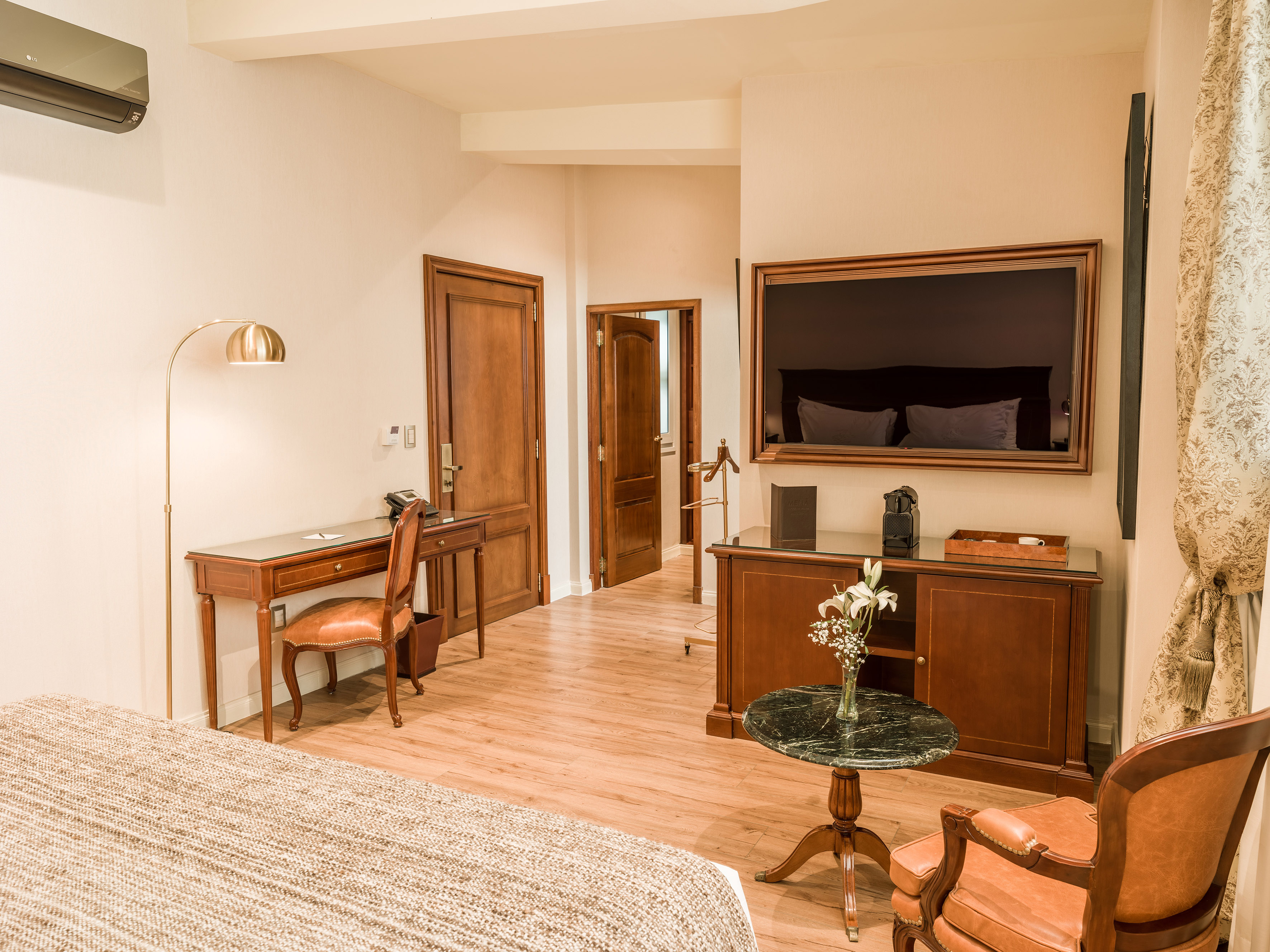 Modern hotel suite featuring a desk, flat-screen TV, and elegant furnishings.