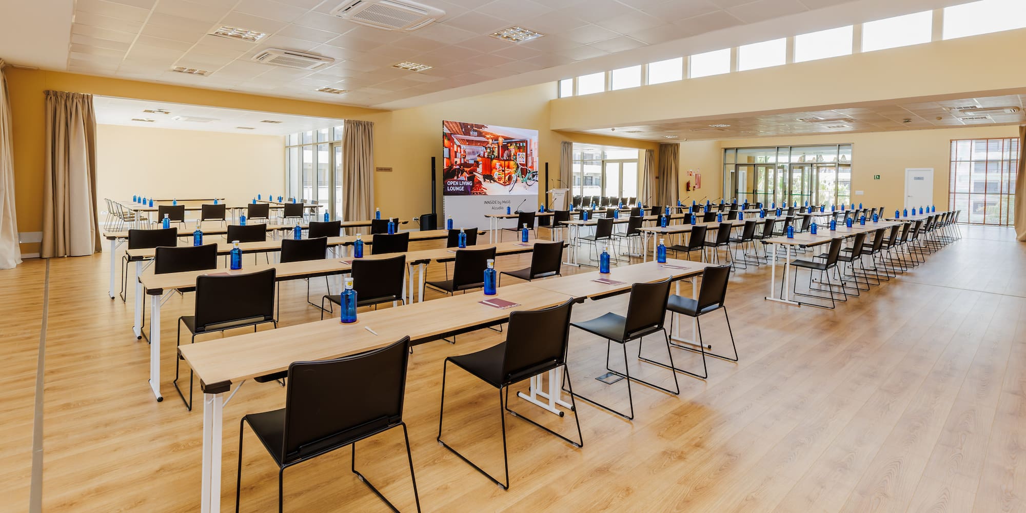 Spacious modern conference room with rows of tables, chairs, and large screen.