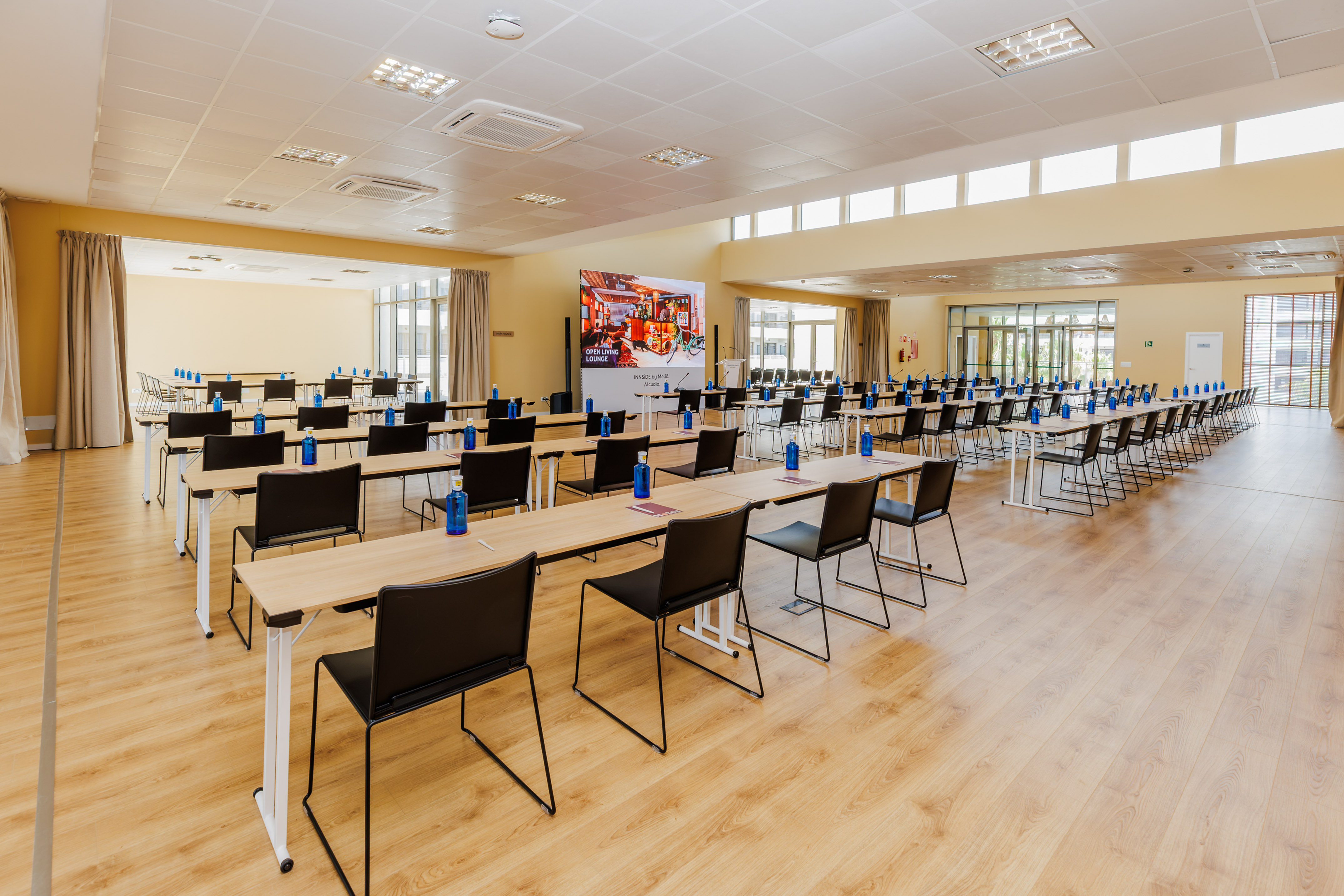 Spacious modern conference room with rows of tables, chairs, and large screen.