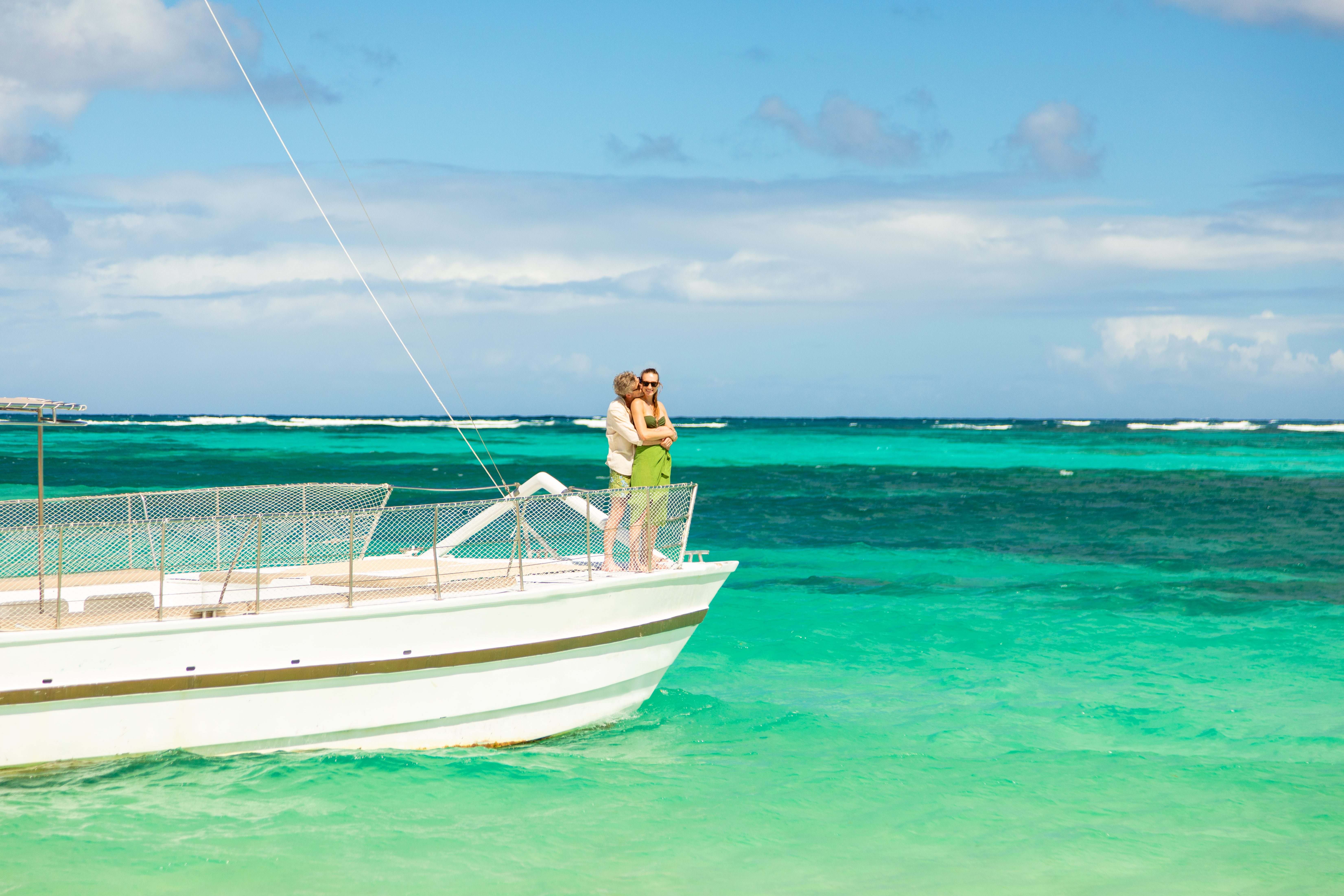 Couple embracing on white boat in vibrant turquoise tropical ocean.