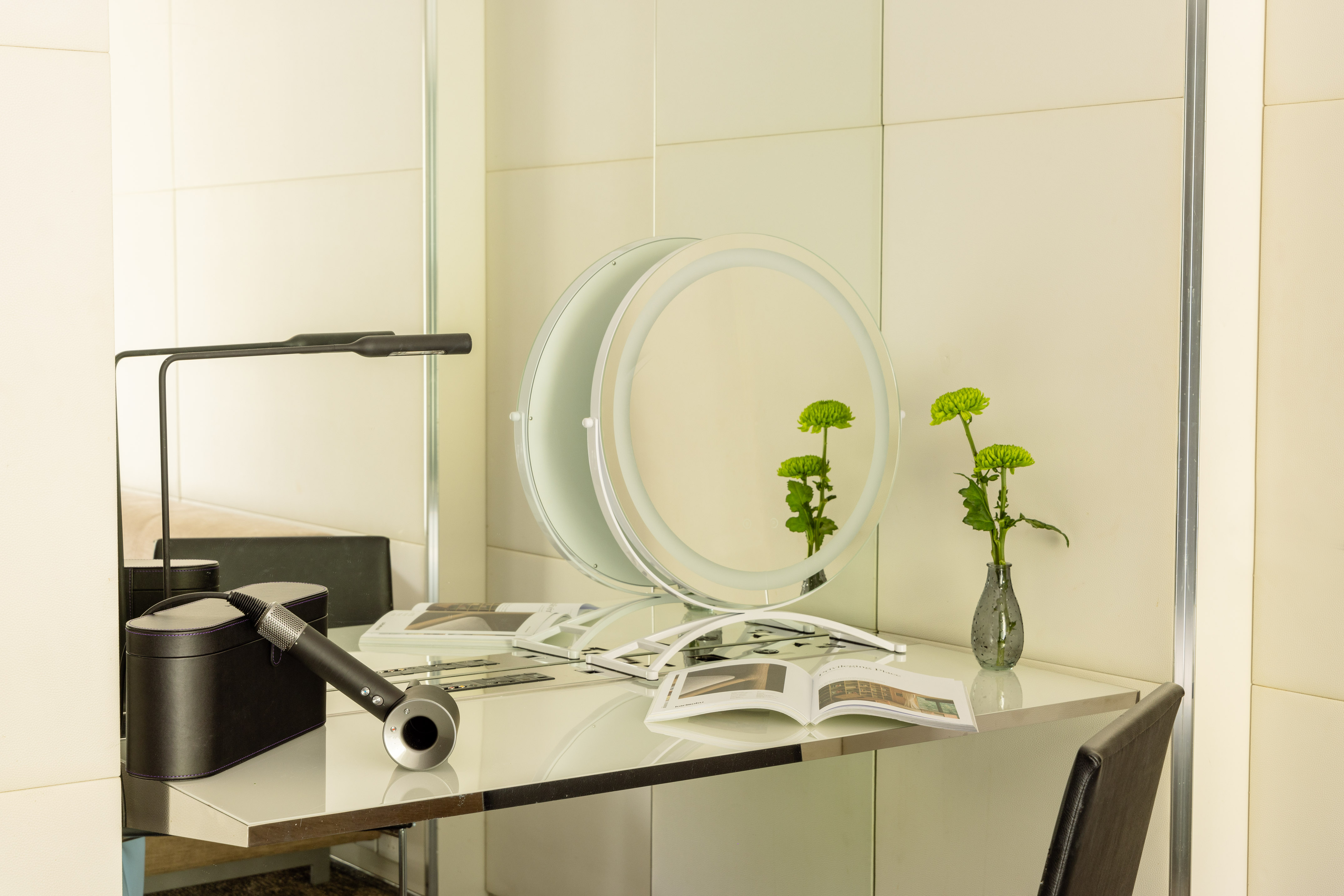 Modern vanity desk with lighted makeup mirror, Dyson hair dryer, and green flowers.