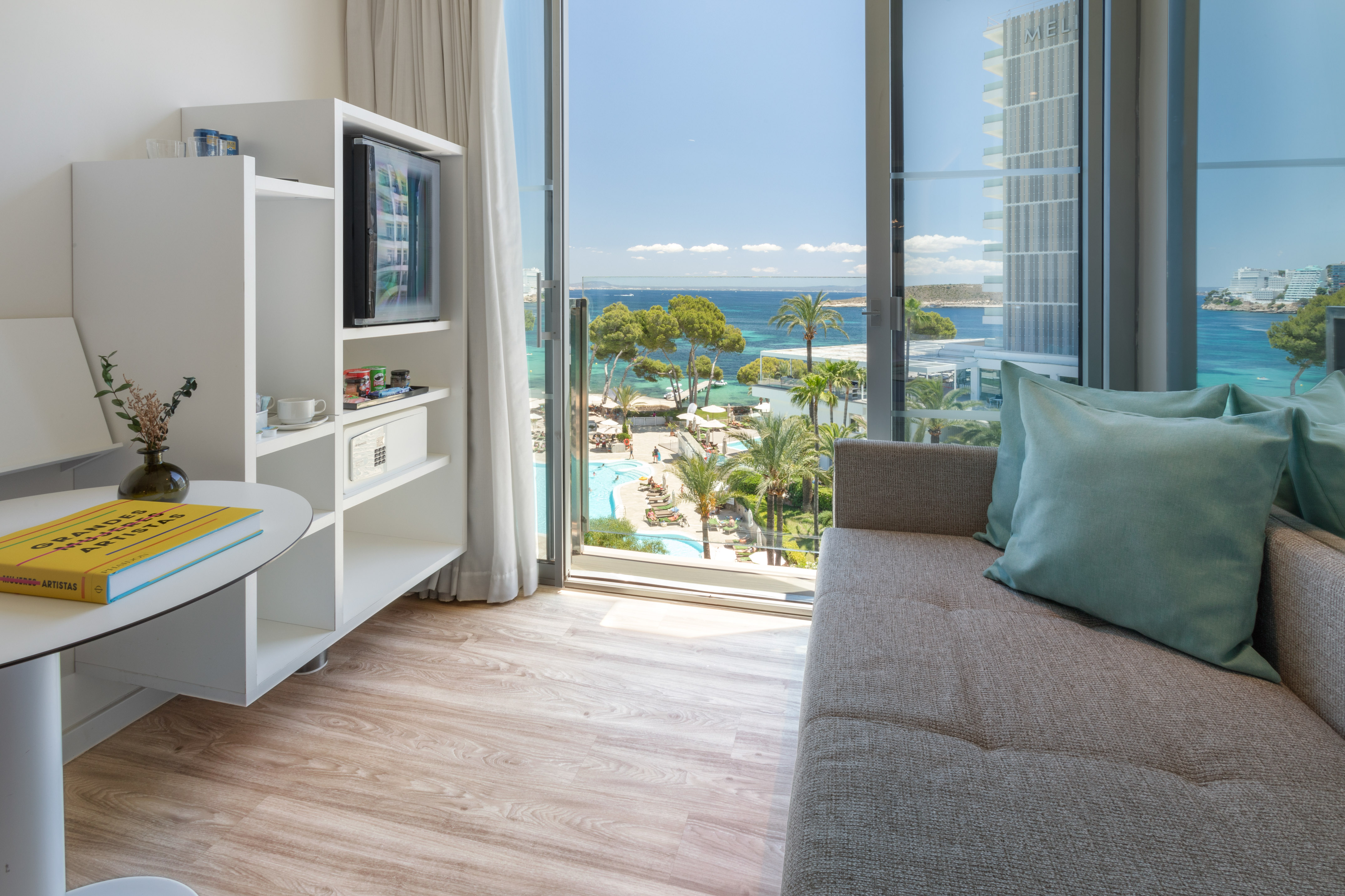Bright hotel room overlooking a resort with beach, ocean, and palm trees.